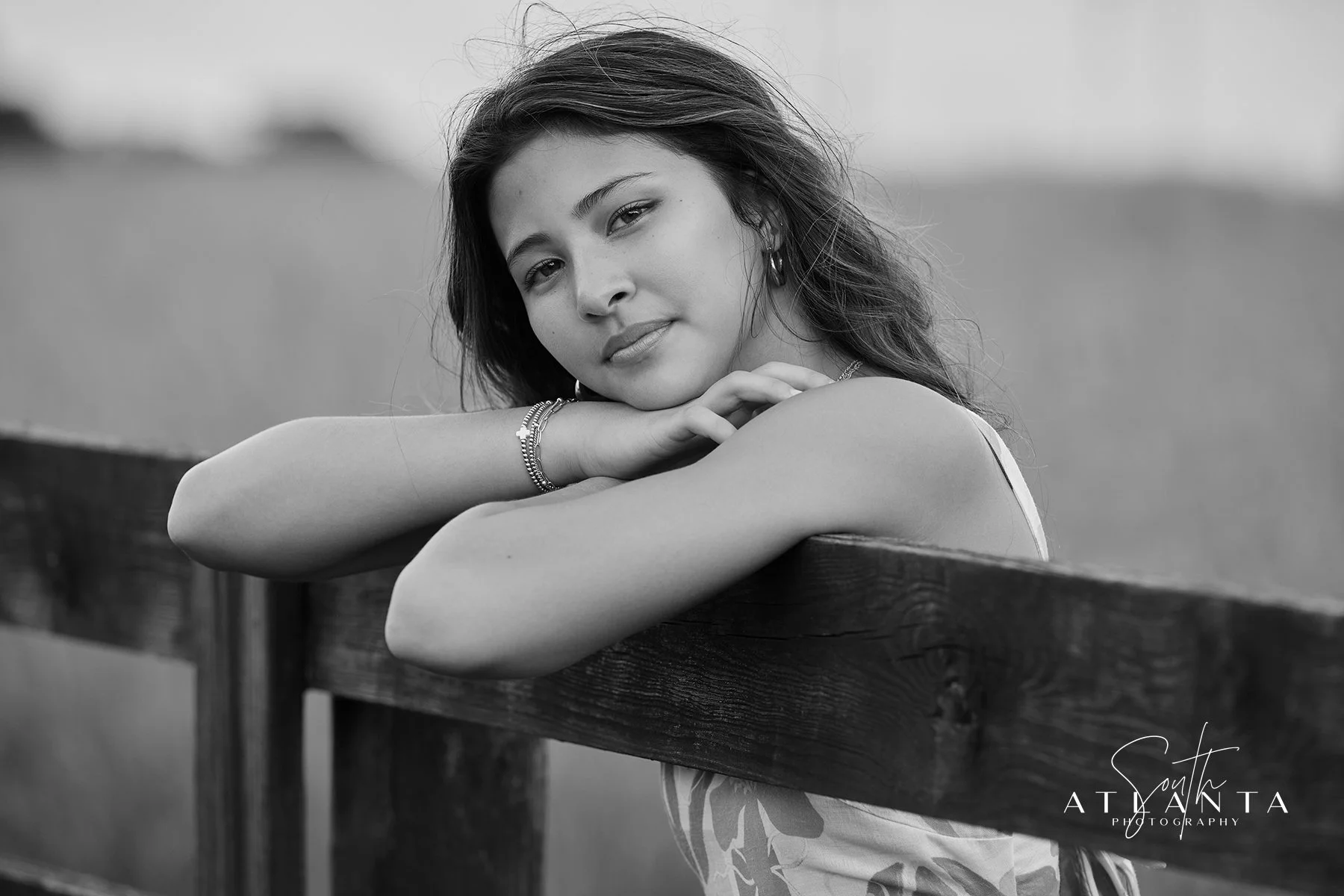 Black-and-white senior portrait of a young woman leaning on a wooden fence during her Wild Daisy Farm senior session by South Atlanta Photography