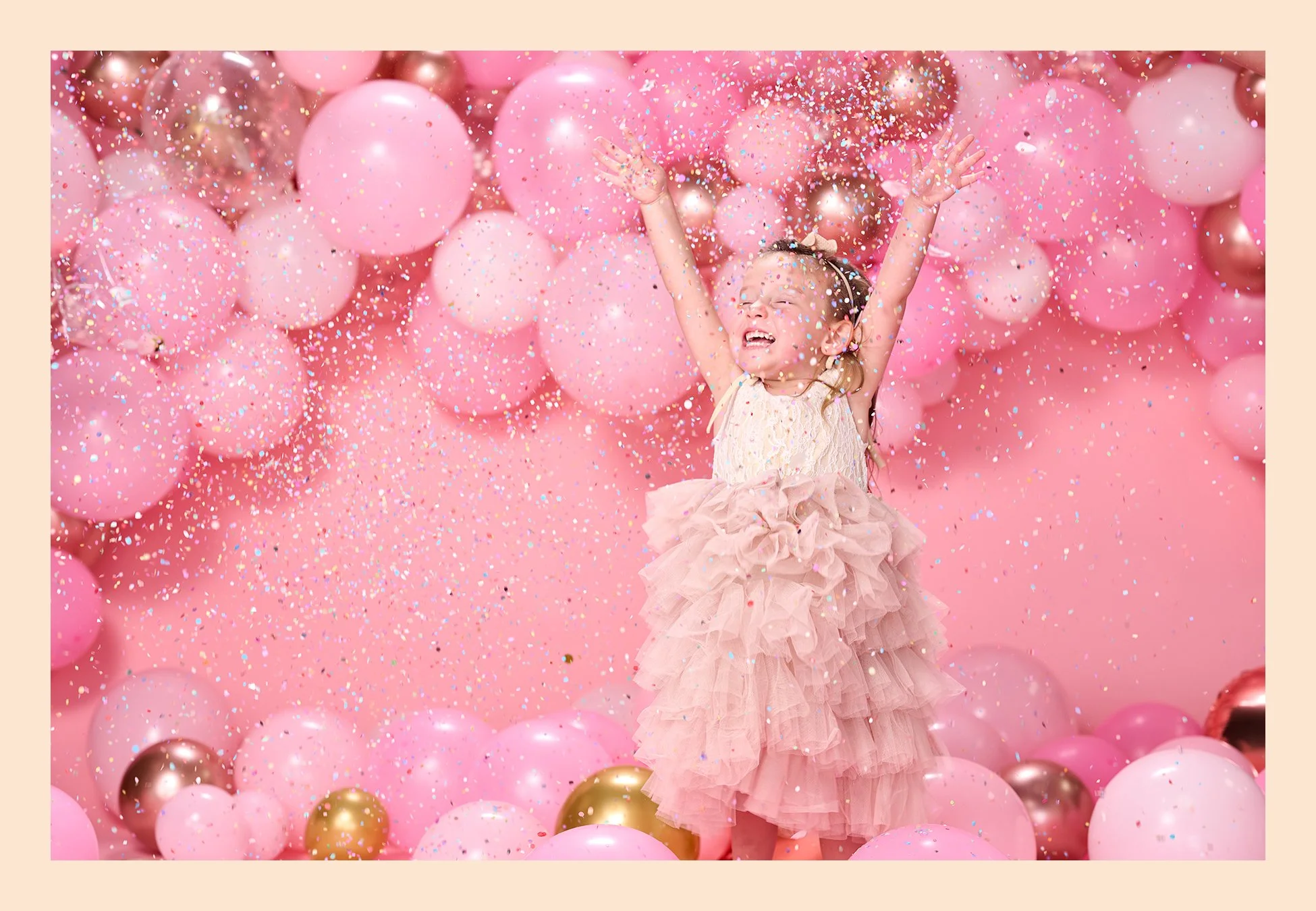 Four-year-old girl throwing colorful confetti into the air while standing among pink, white, and metallic balloons during her fourth birthday portrait session.