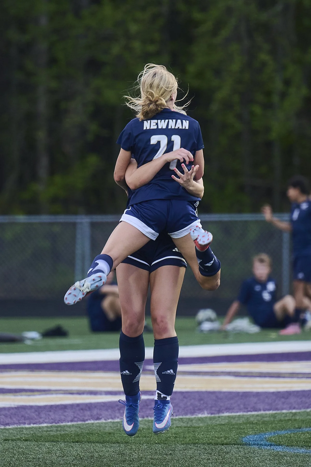 Two Newnan high school girls soccer players celebrate on the field, with one player jumping into her teammate’s arms after a moment during the game.