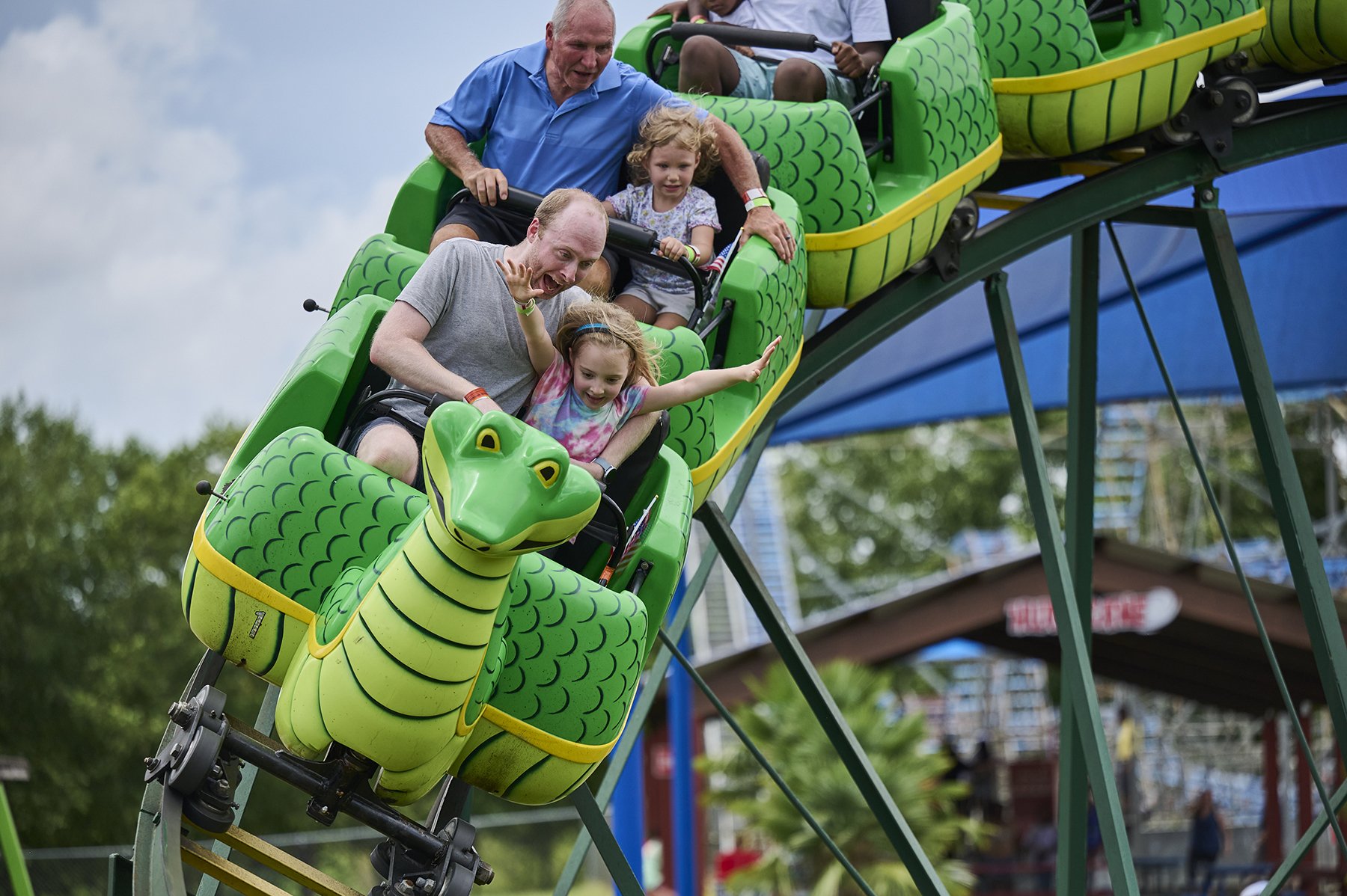 Adults and children riding a green dragon roller coaster together at Fun Spot Amusement Park during a family reunion outing at an amusement park.