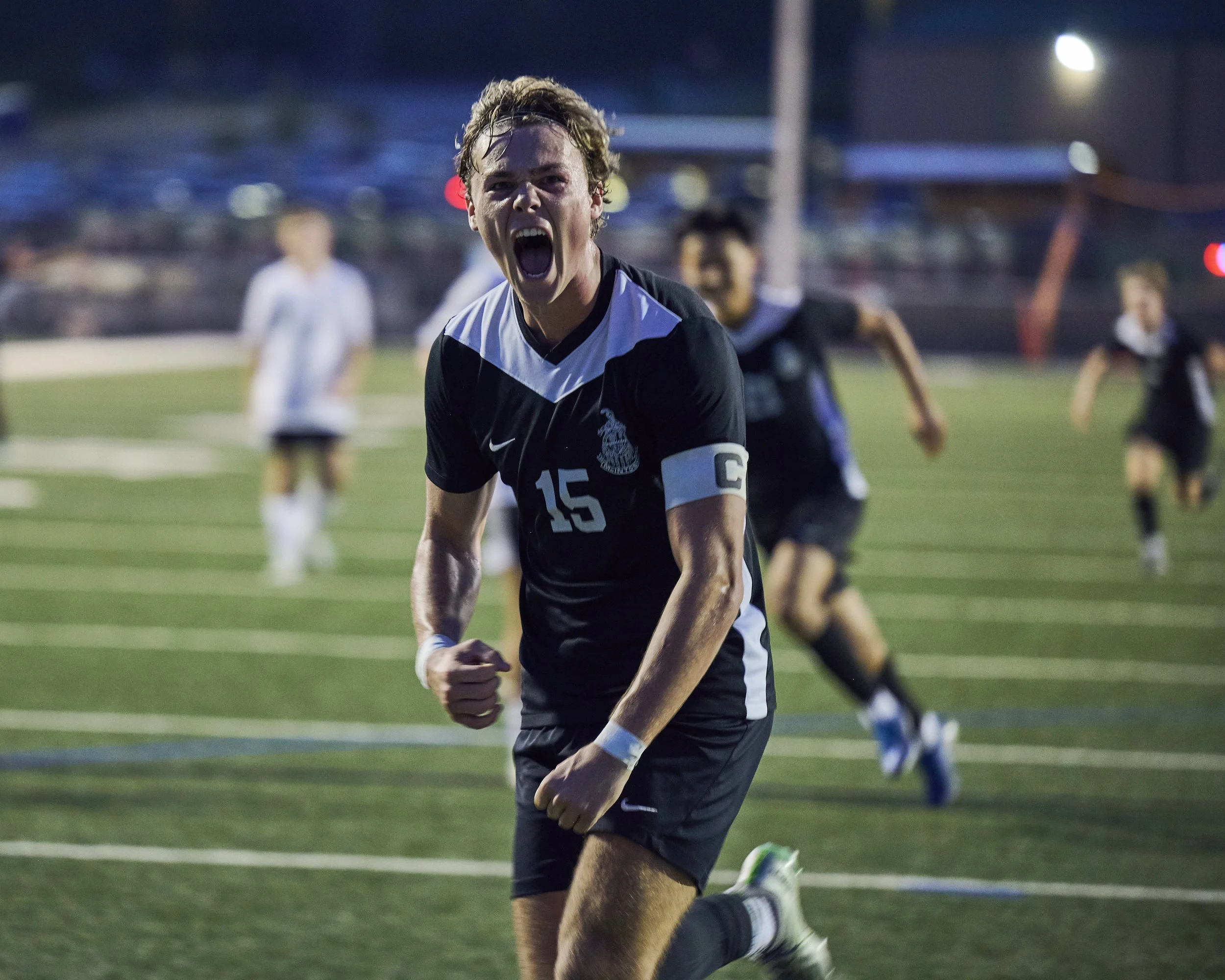 High school soccer player wearing number 15 celebrates intensely on the field during a night game in Peachtree City, Georgia.