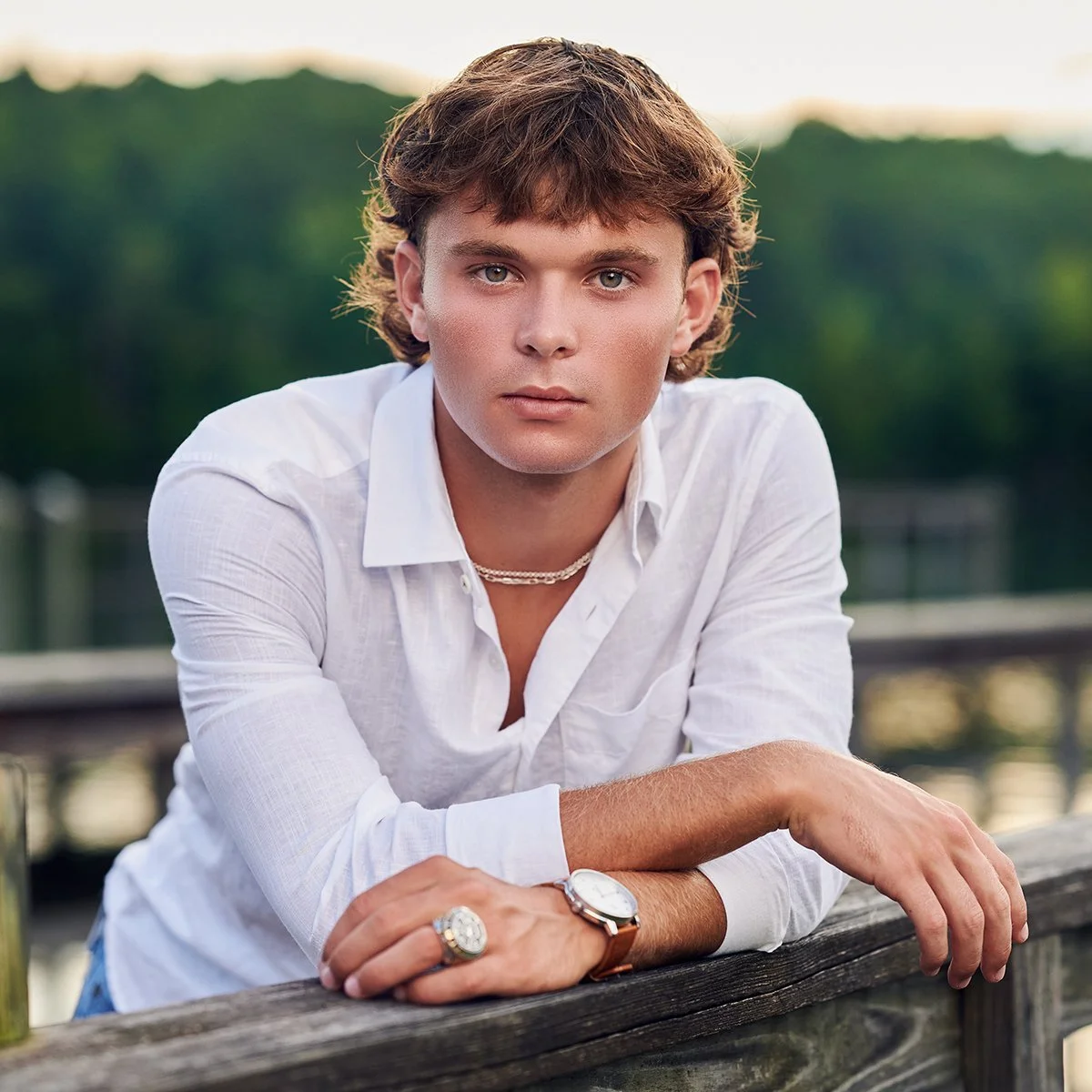Senior guy in a white button-down shirt leaning against a lakeside railing during an outdoor senior portrait session in Peachtree City, Georgia.