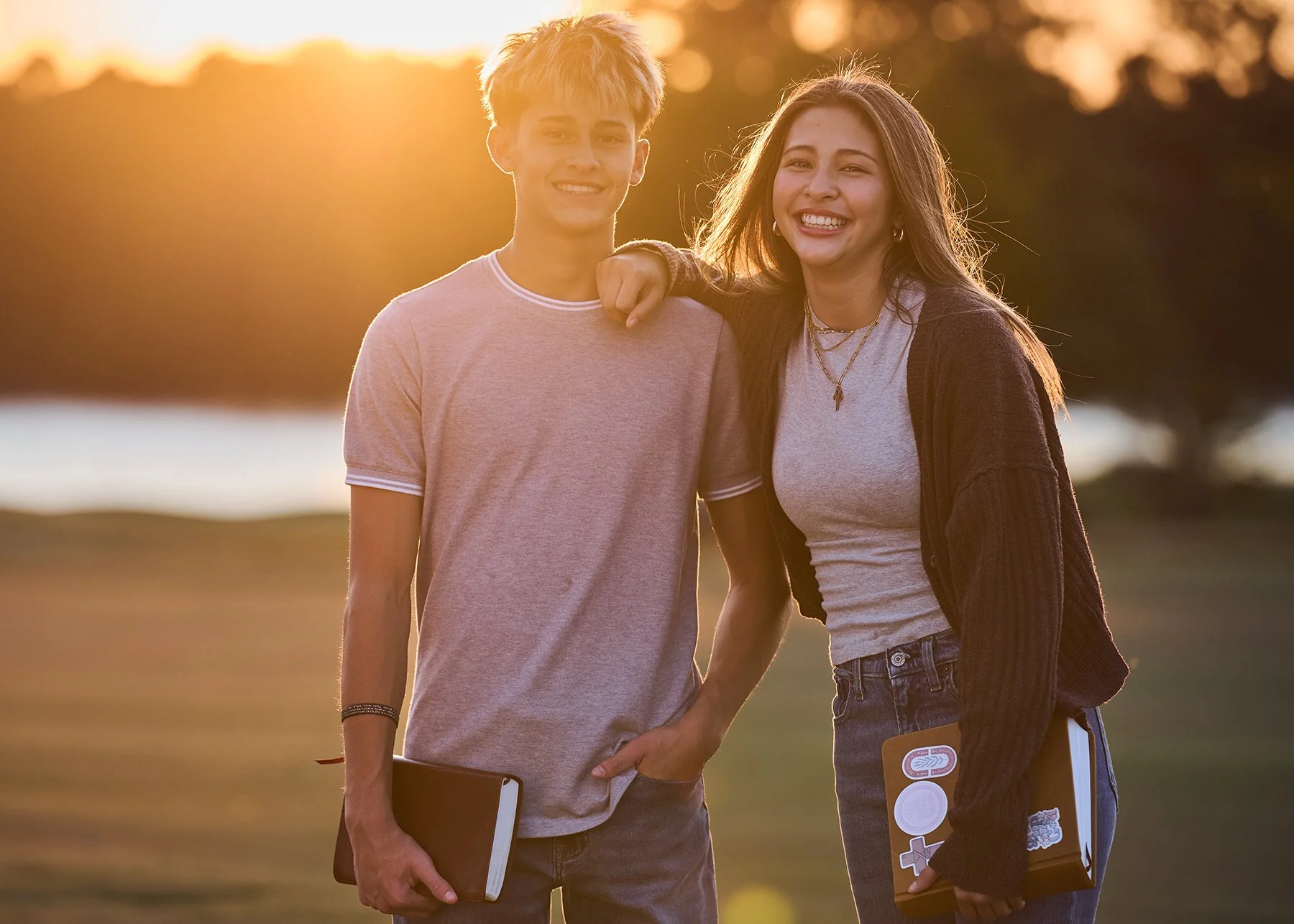 Twins, high school seniors smiling at sunset by Lake McIntosh in Peachtree City, holding books during a golden hour portrait session