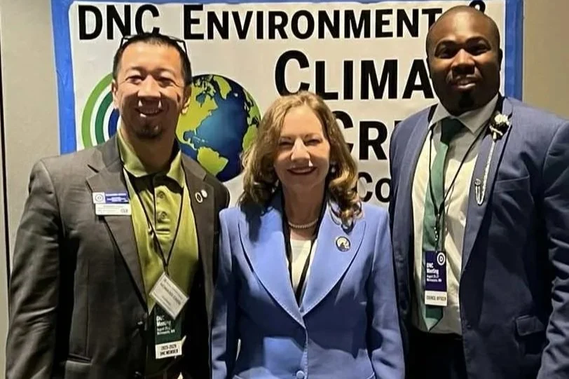 Three people face the camera, smiling, wearing business suits.