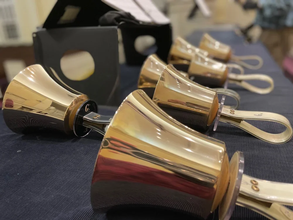 A row of shiny brass bells with white handles laid out on a dark fabric surface, with a black box in the background.