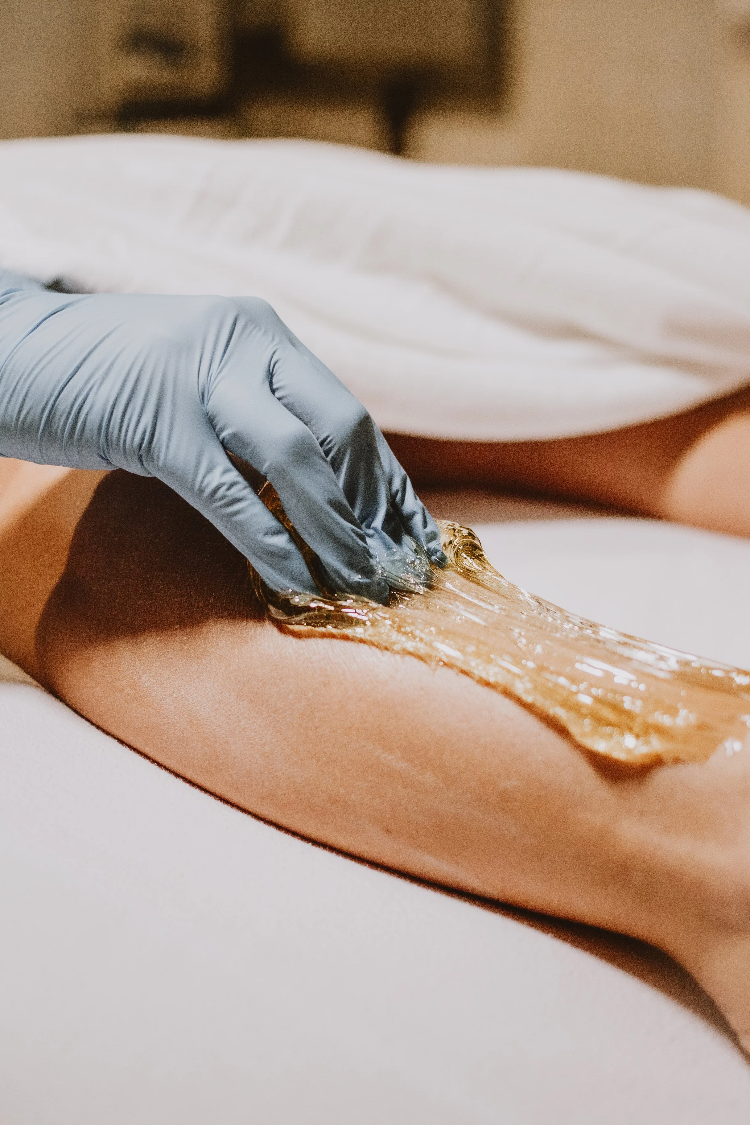 A person receiving a gold wax hair removal treatment on their leg, with a gloved hand applying the wax.