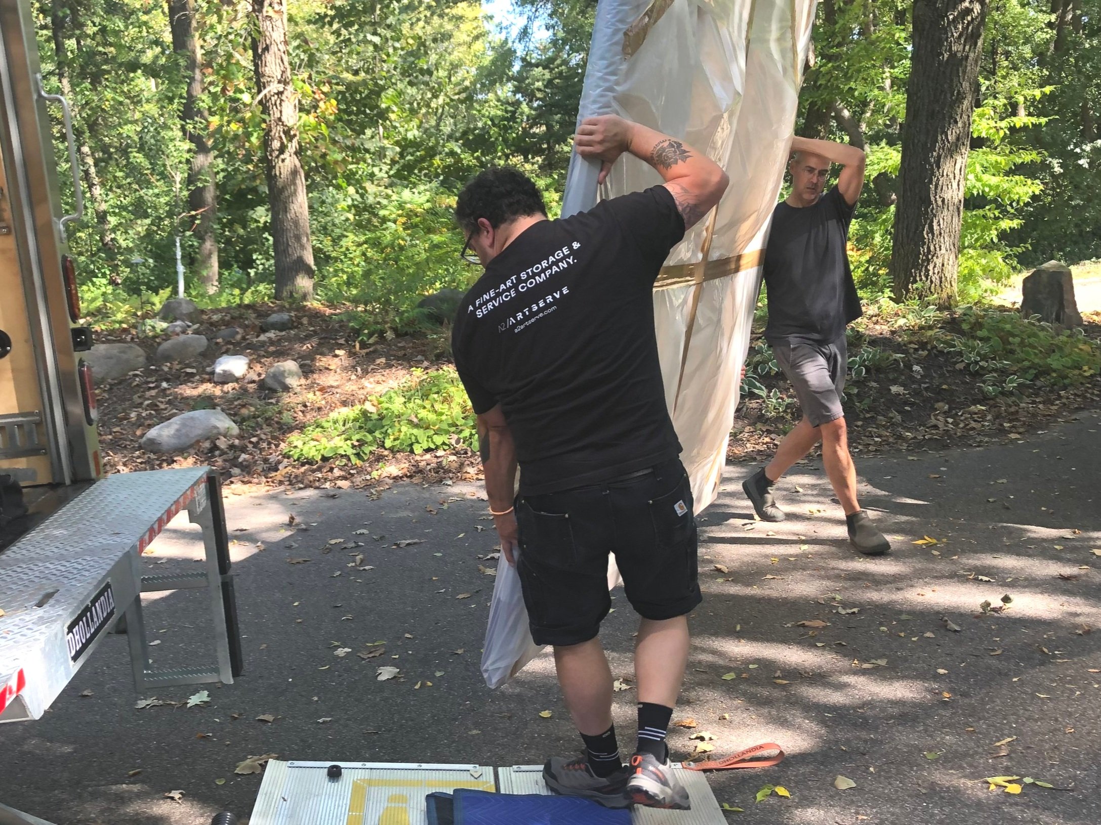 Two art handlers wrapped an oversized artwork and are carrying it into a truck for transportation