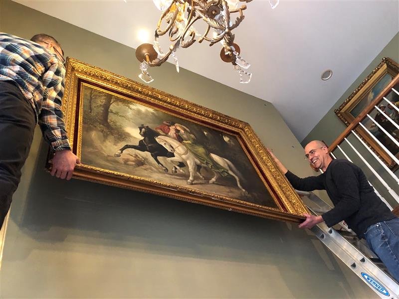 Art handlers installing fine art together in a home
