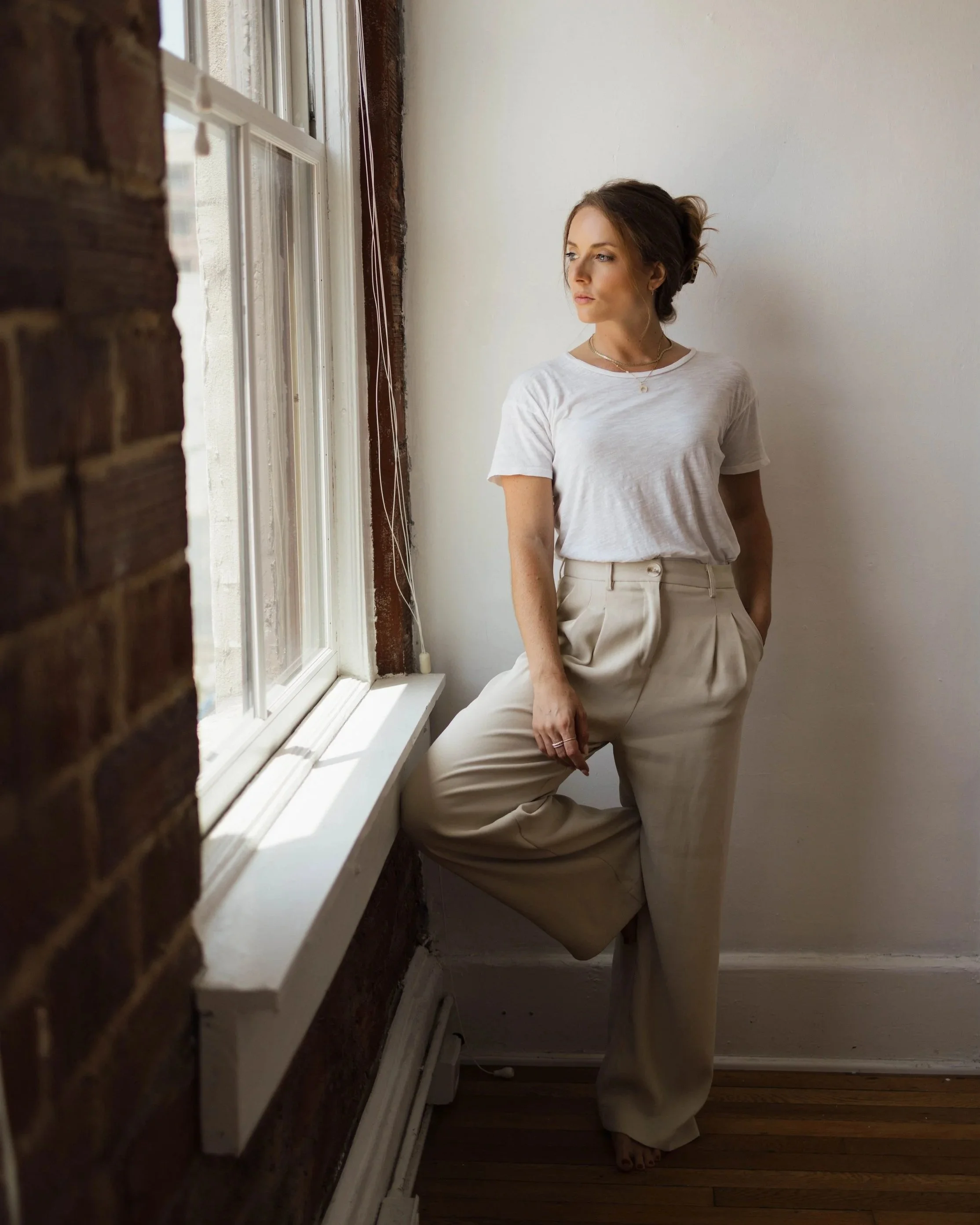 Woman in cream-colored outfit practicing yoga in a child’s pose on a hardwood floor