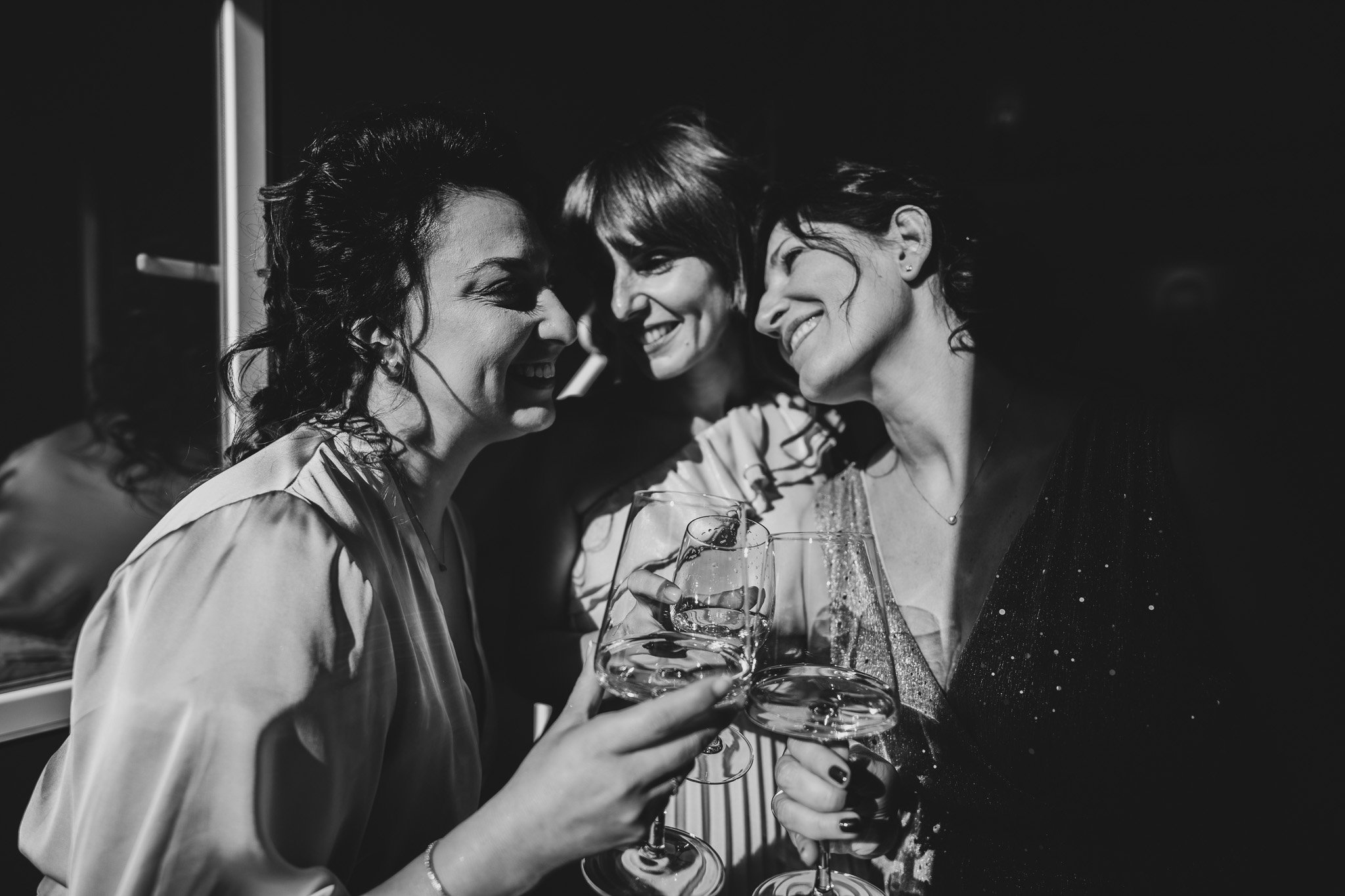 Tre donne sorridenti tengono bicchieri di vino e brindano durante una festa in un ambiente elegante.