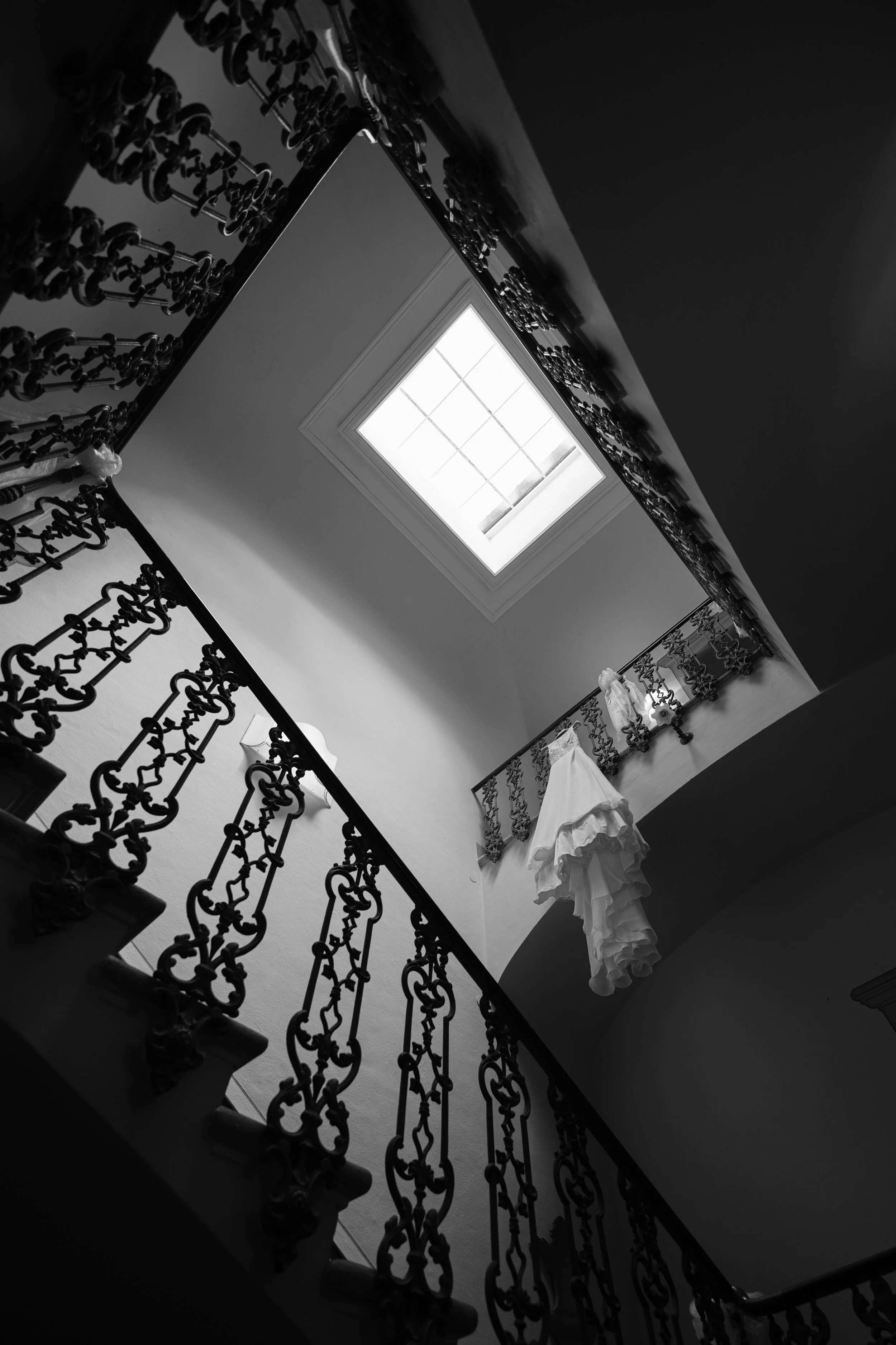 Immagine in bianco e nero di una soffitta con un lucernaio, una ringhiera decorativa e alcuni vestiti appesi.