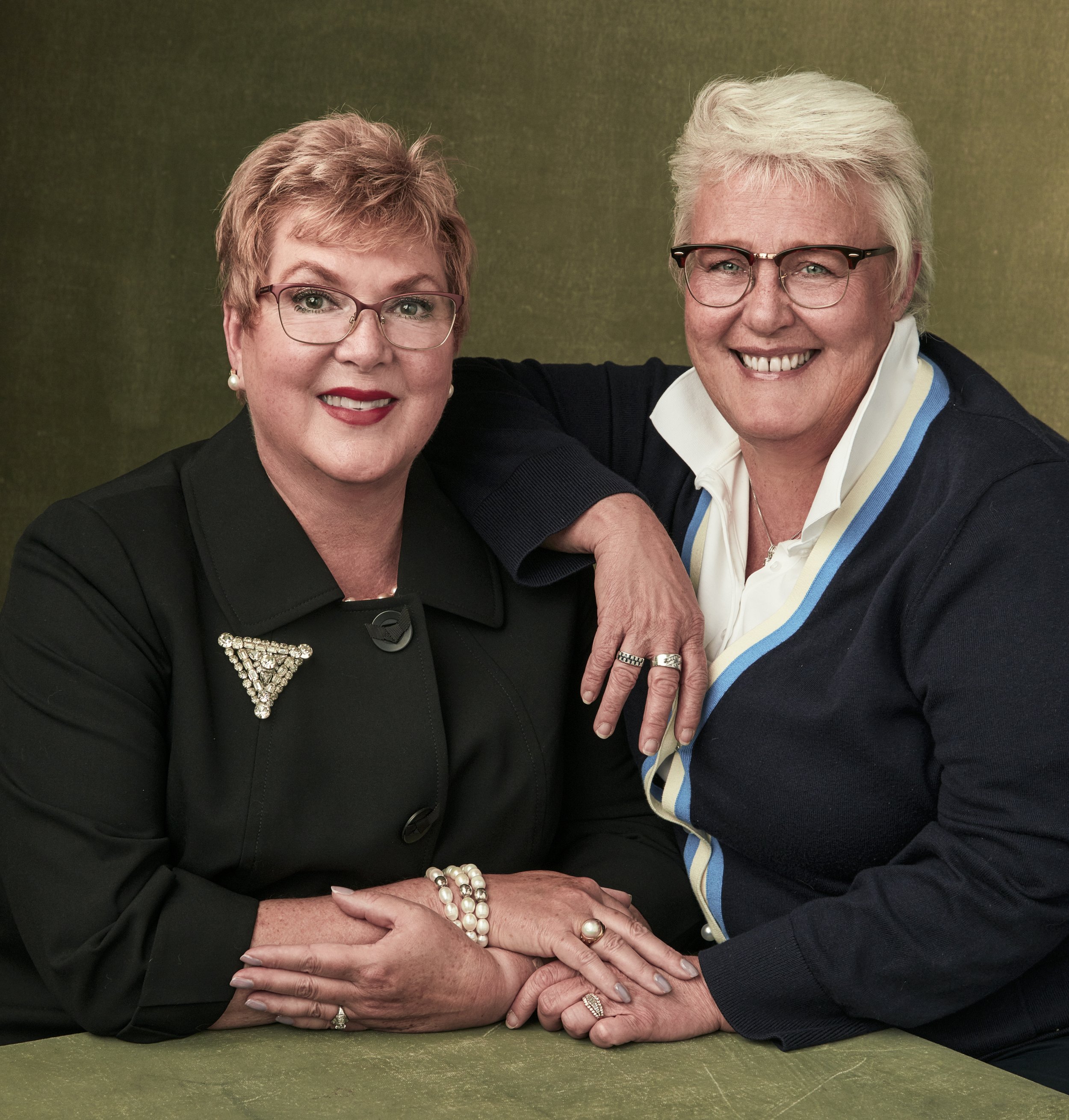 Portrait of two older women both dressed in smart professional attrie posed in front of a neutral backdrop