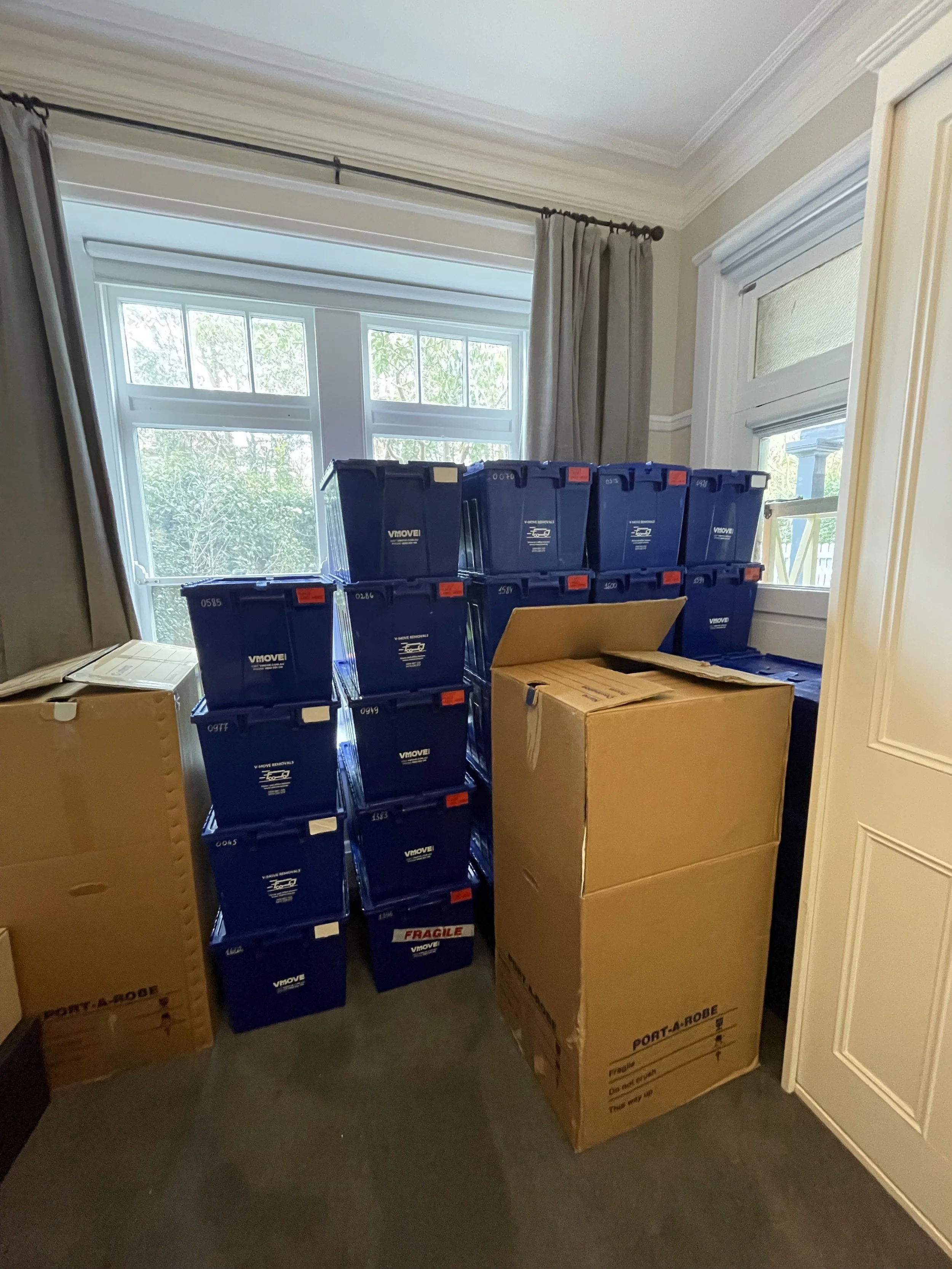 Stack of blue and cardboard moving boxes in front of windows.
