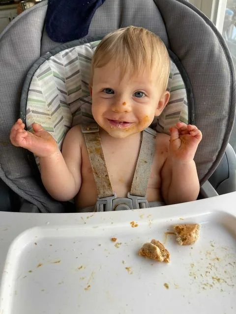10 month old boy smiling and eating toast in a highchair