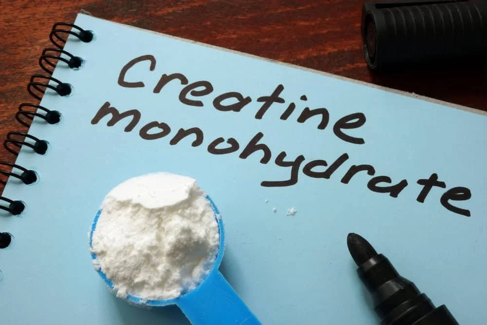 Scoop of creatine monohydrate powder next to notebook and pen