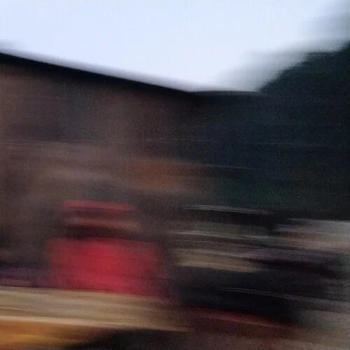Blurry image with indistinct shapes and colors, possibly outdoors or in low-light conditions.
