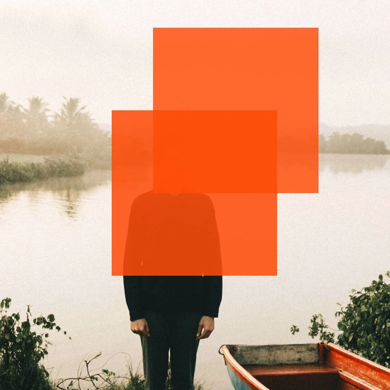 A person standing by a river with tropical trees in the background, partially obscured by red rectangles, next to a small boat.