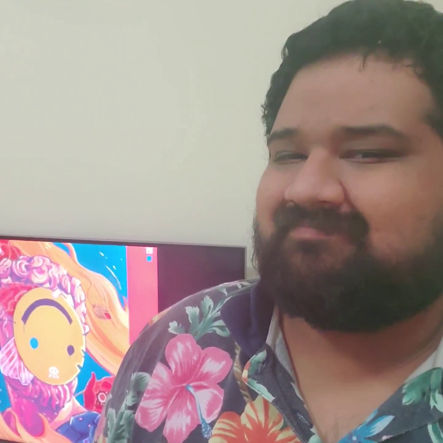 A person with a beard wearing a floral shirt stands in front of a computer screen displaying colorful cartoon artwork.