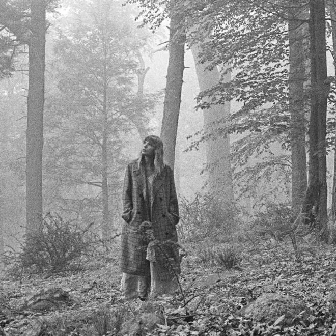 Person standing in a foggy forest, wearing a long coat.
