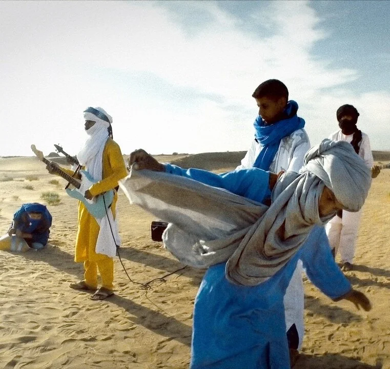 People in traditional Berber clothing performing music in a desert setting.