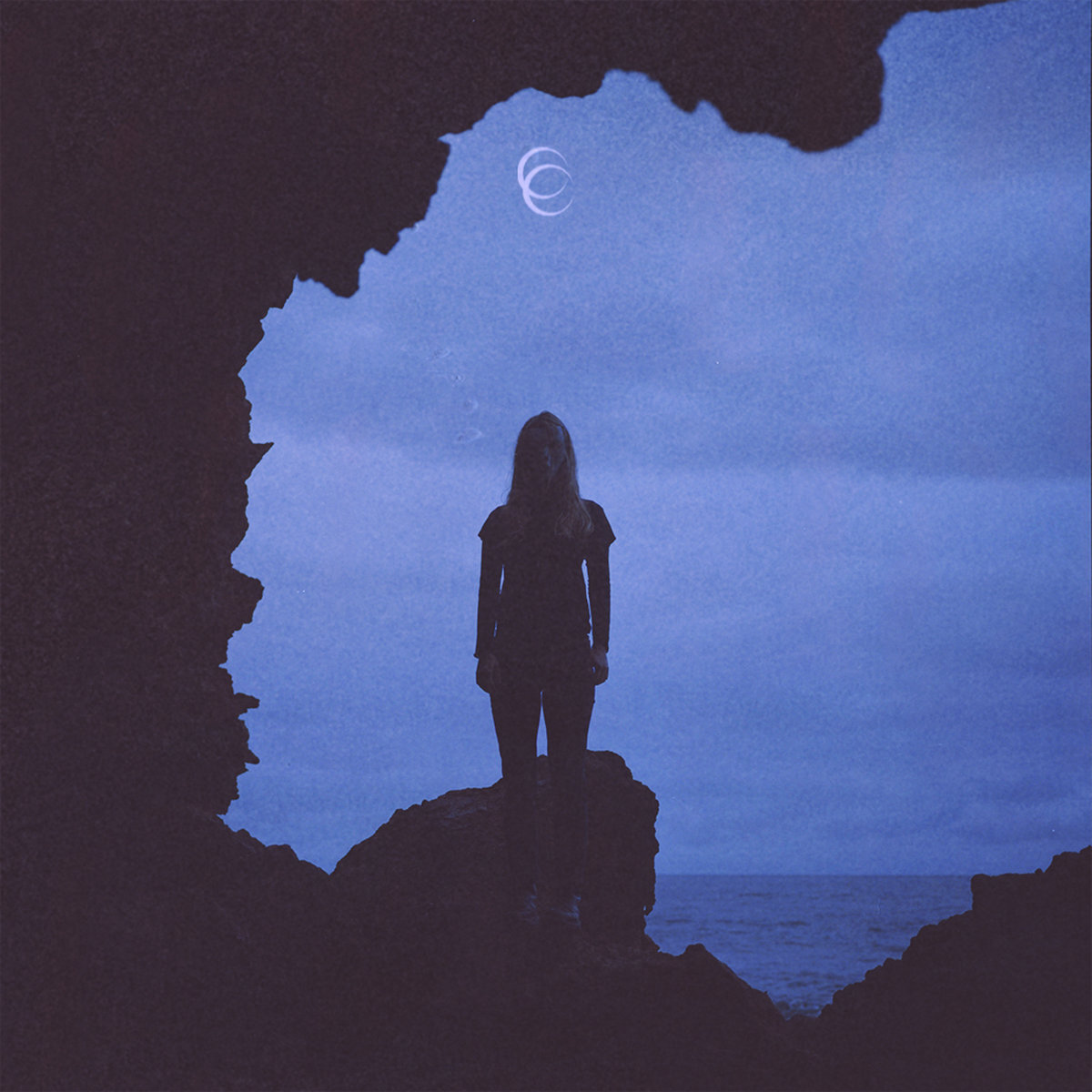 Silhouette of a person standing on rocks against a blue sky with a crescent moon emblem.