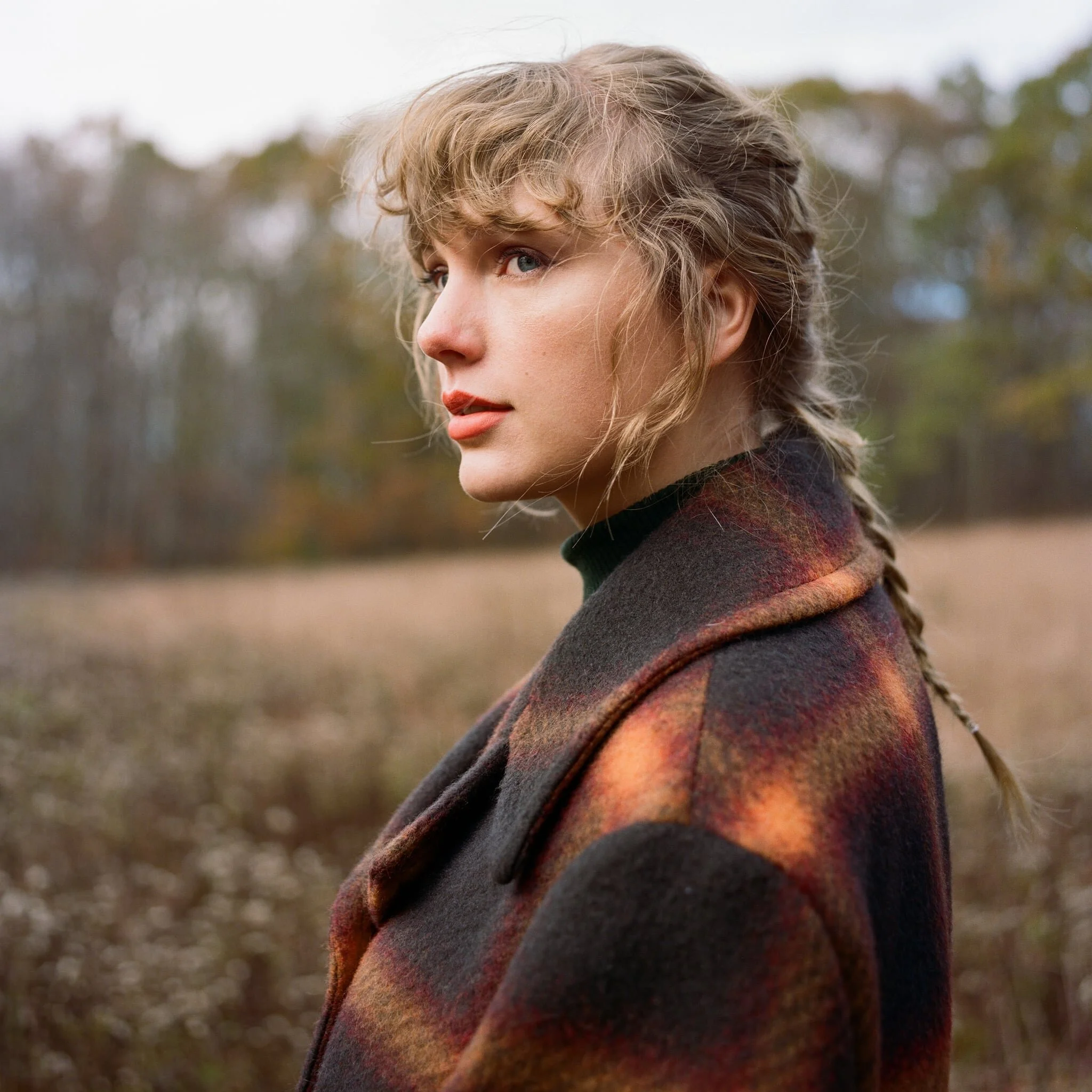 Woman with braided hair wearing a plaid coat in a field