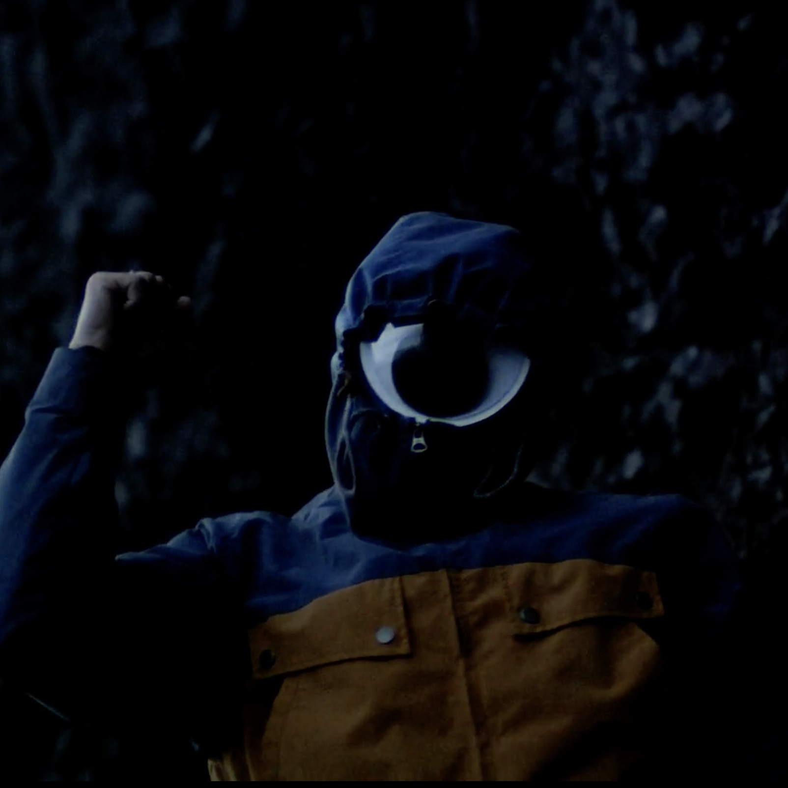 Person in hooded jacket with large eye symbol in dim lighting.