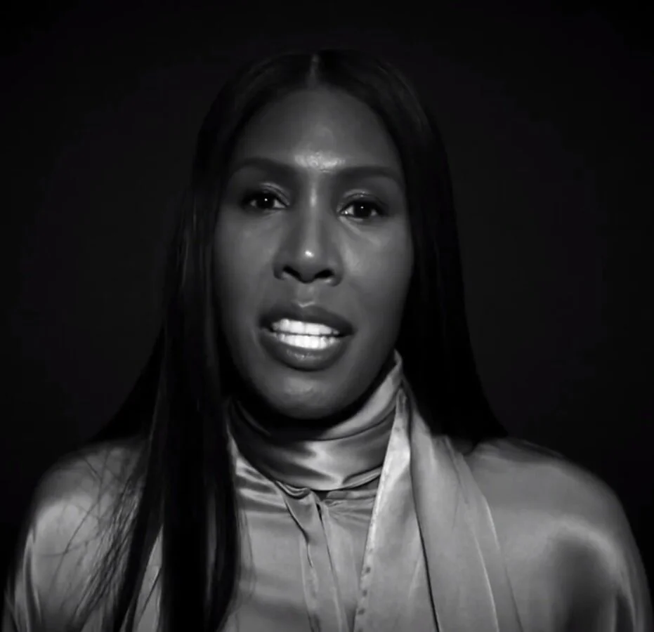 Black and white portrait of a person wearing a silk shirt, looking towards the camera with a neutral expression.