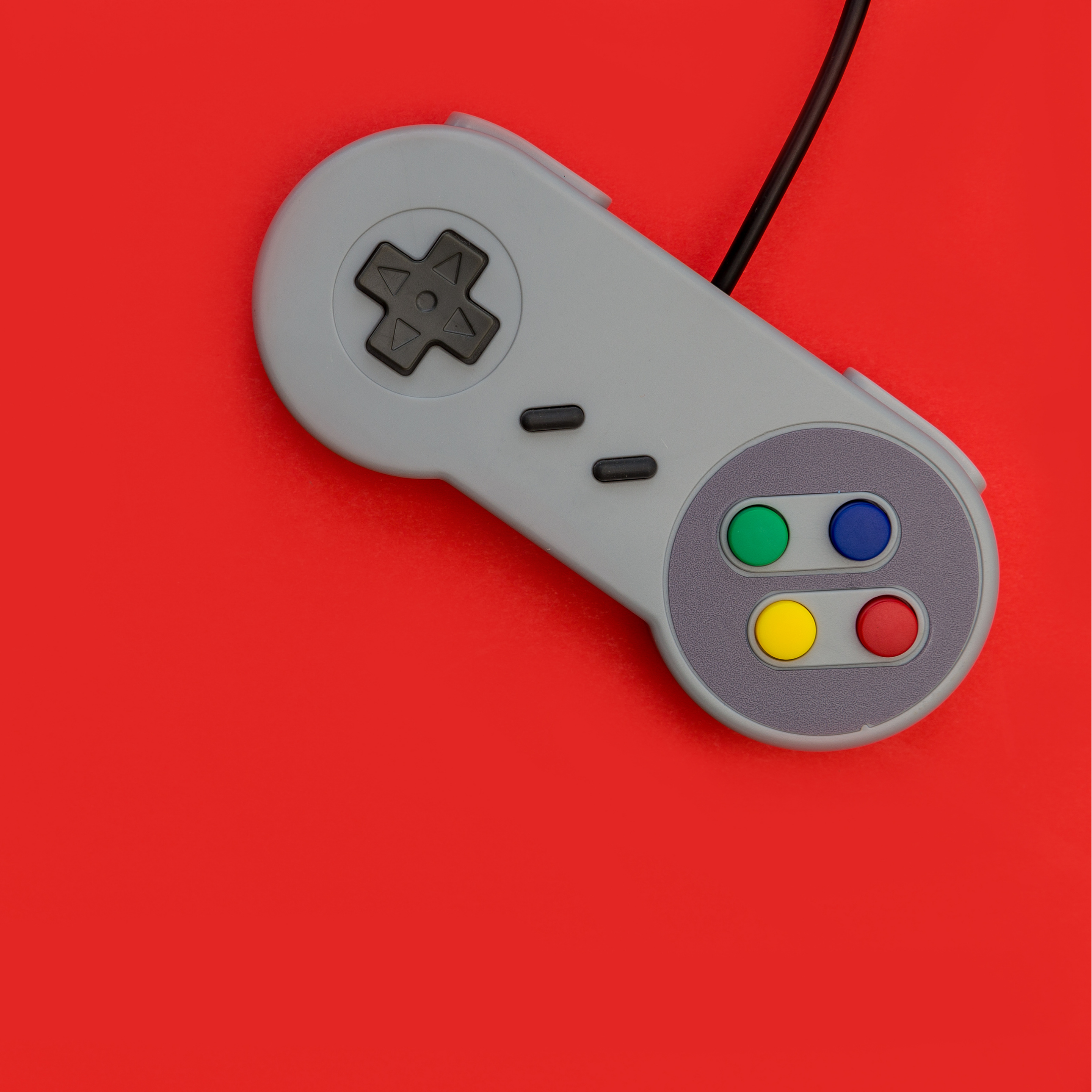 Gray gaming controller with colorful buttons on a red background