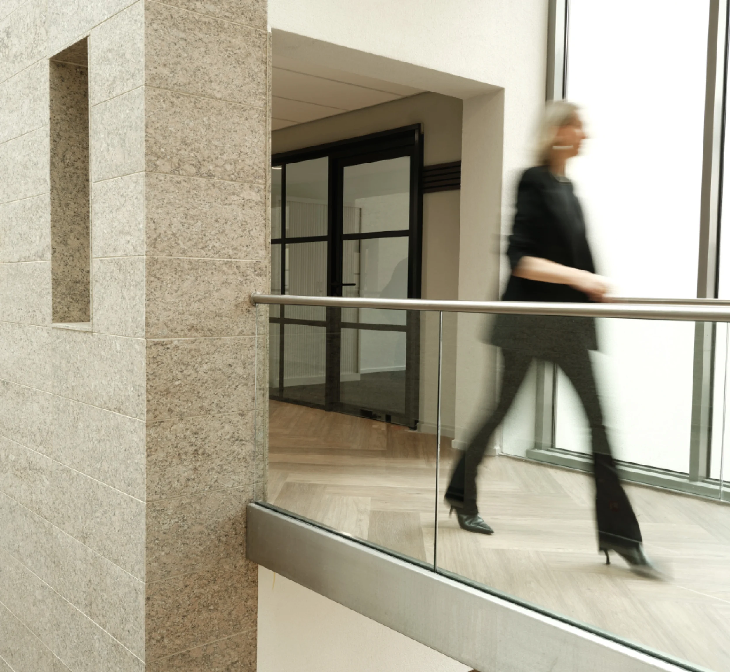 Vrouw in nette donkere kleding die snel over een loopbrug loopt.