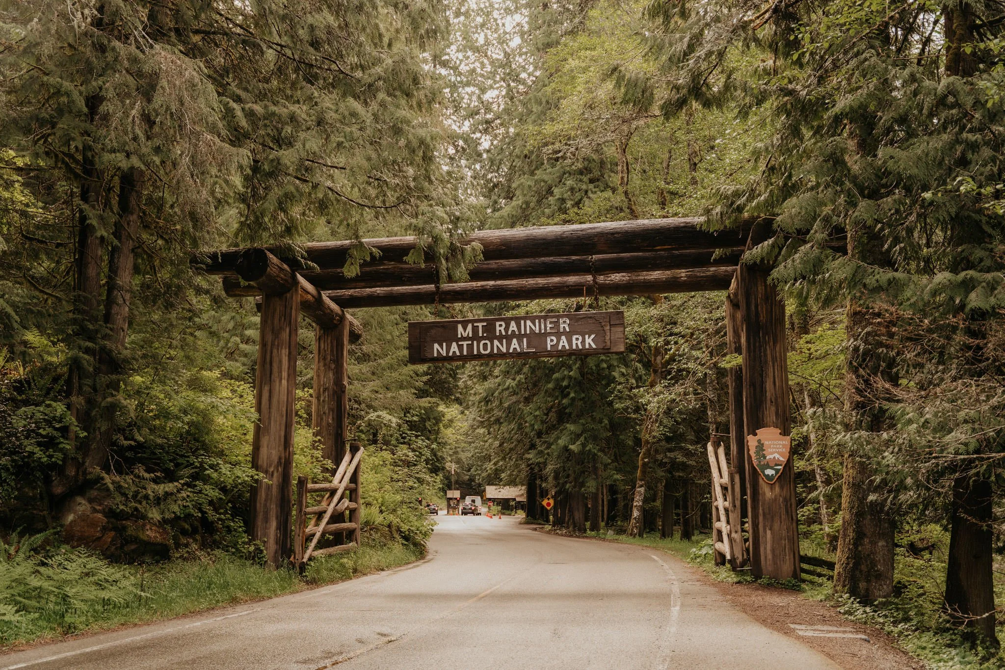 Wooden archway with a sign reading 'Mt. Rainier National Park' on a forested mountain road.