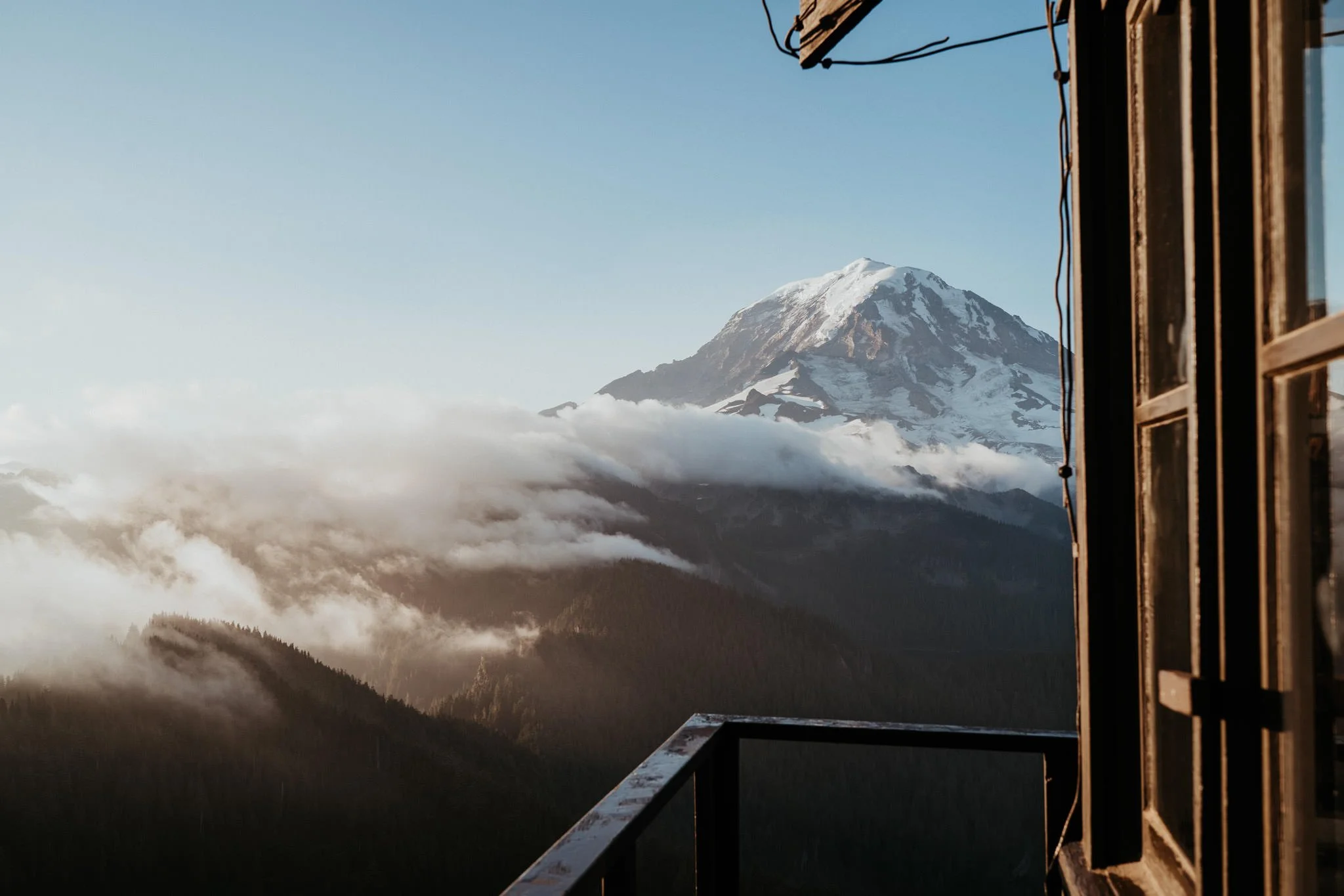 View of Mount Rainier with snow-capped peak seen from a balcony with an open window and safety railing