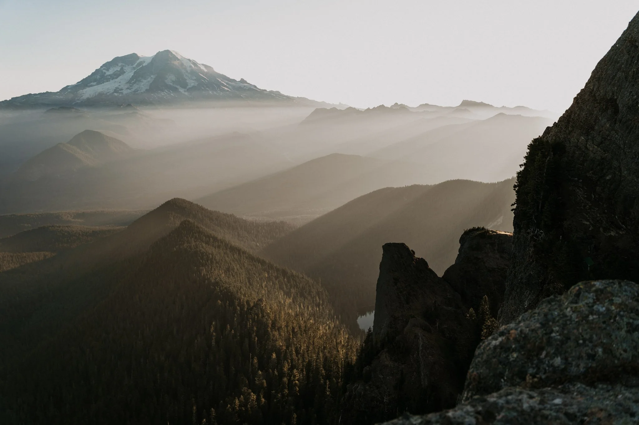 Mountain landscape with forested hills, rocky cliffs, and a snow-capped peak in the distance