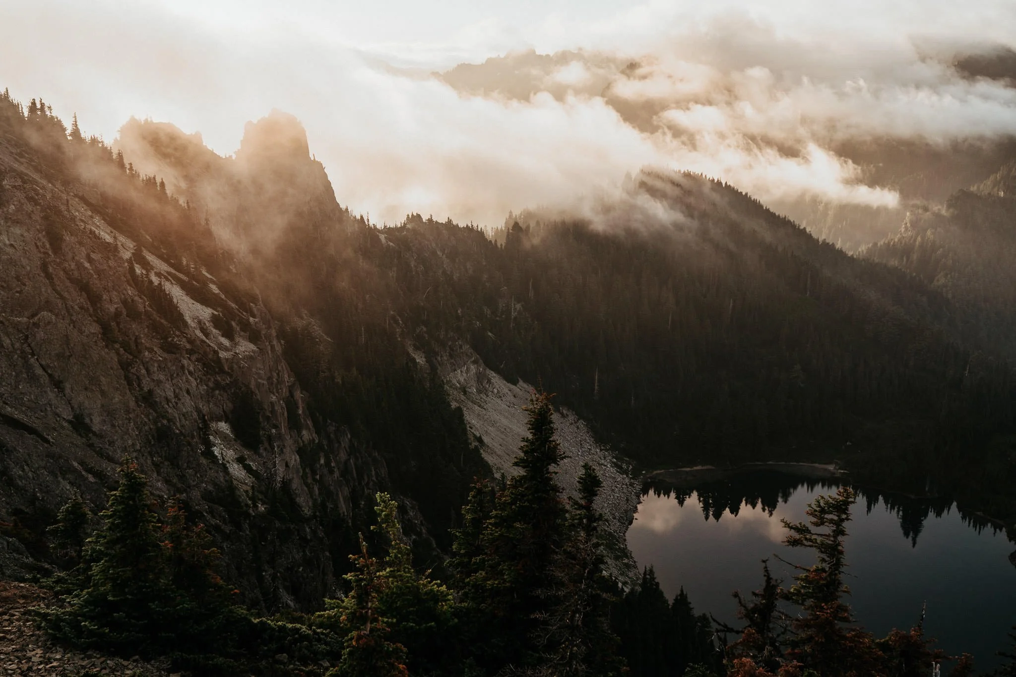 Mountain landscape with forest, cloudy sky, and a lake reflecting the trees and mountains.
