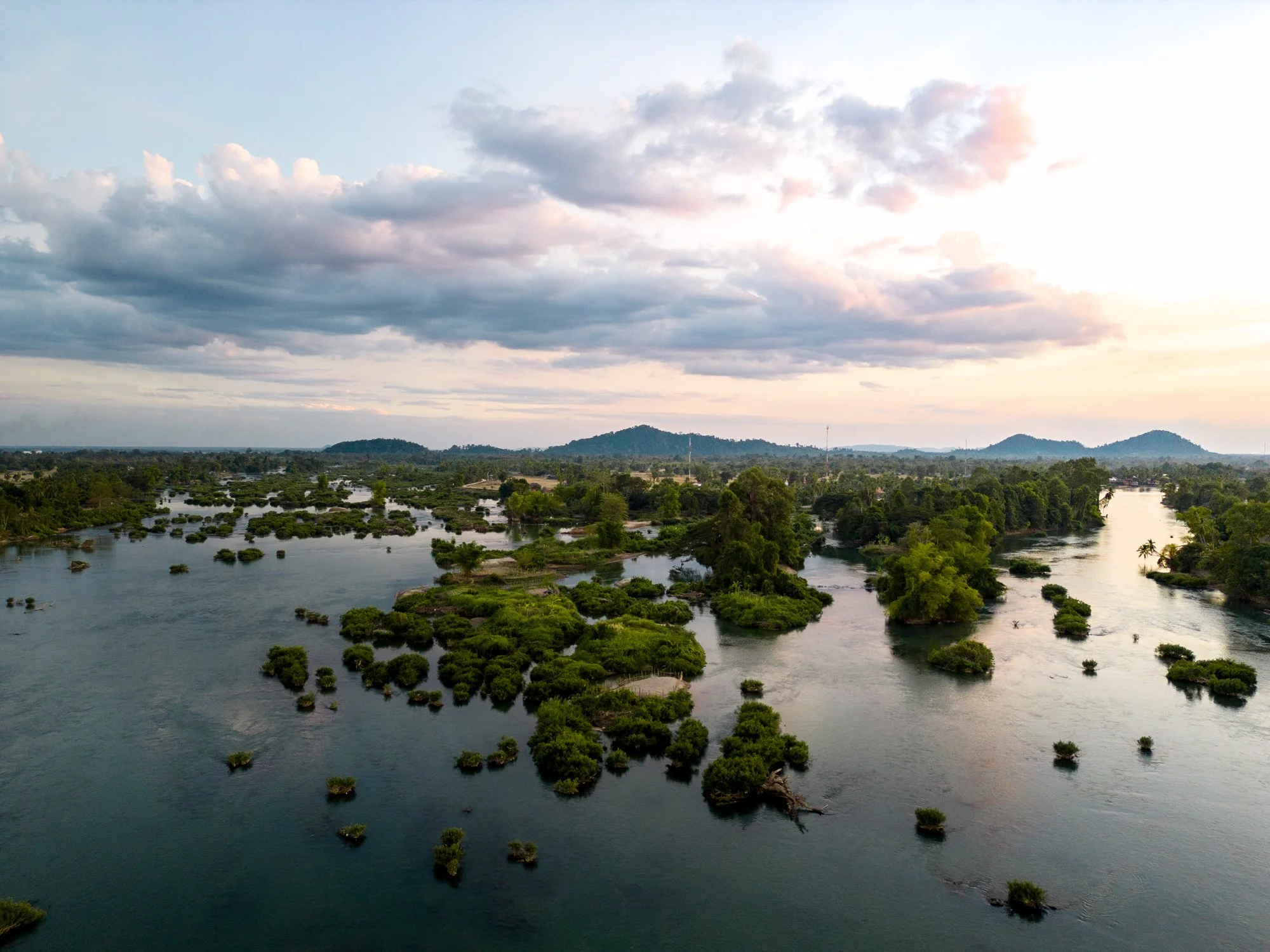 An aerial view of the Mekong river with numerous small islands and green trees, under a cloudy sky at sunset.