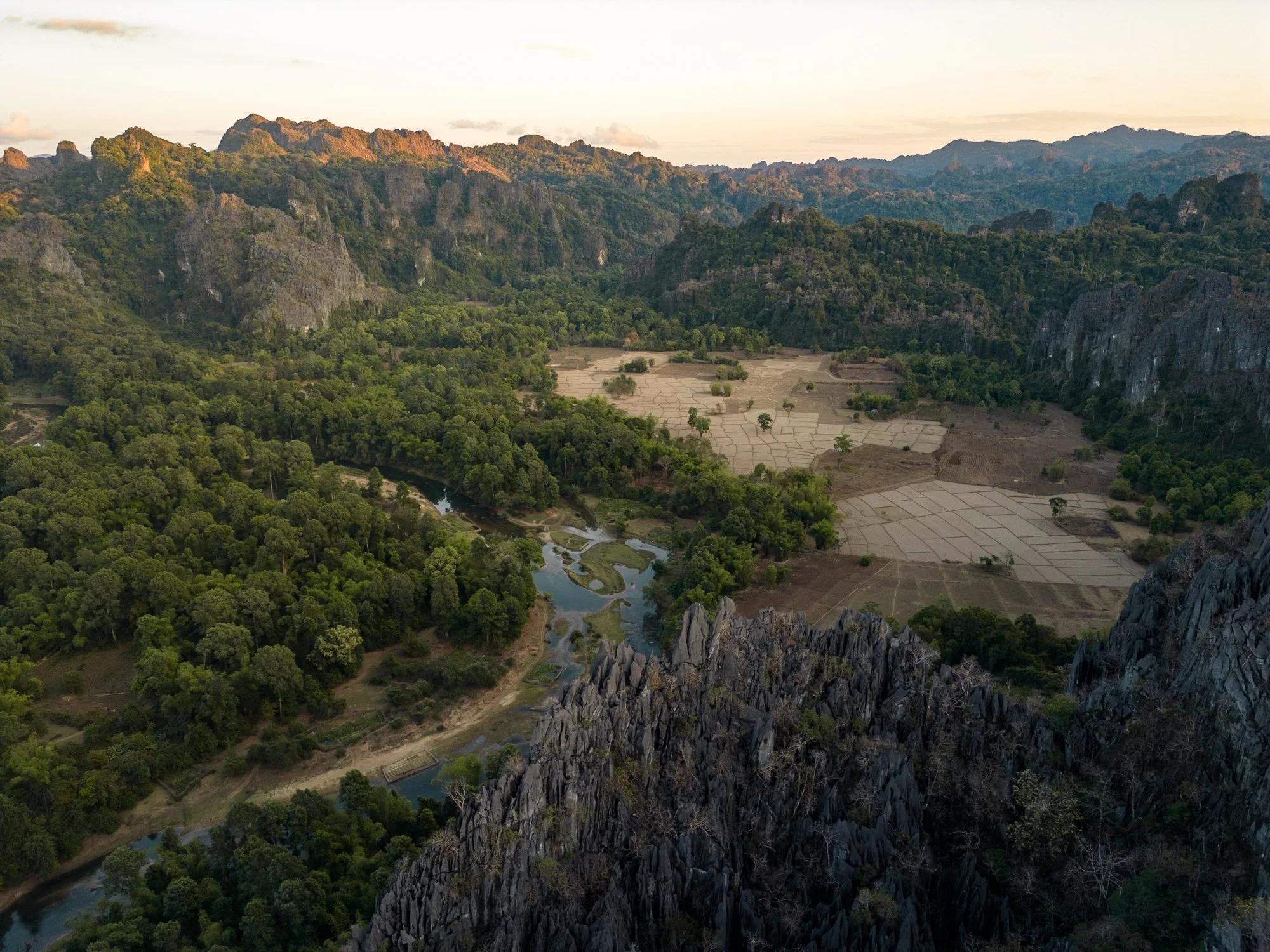 Aerial view of Kong Lor, Laos. A lush green valley with a winding river, surrounding mountains, and agricultural fields.