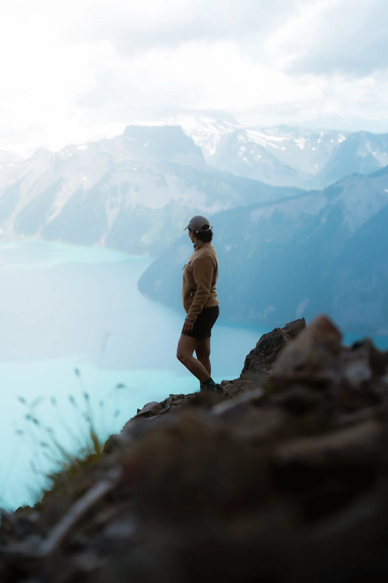 A woman standing on Panorama Ridge overlooking the blue waters of Garibaldi lake and snow-capped mountain range in the distance.
