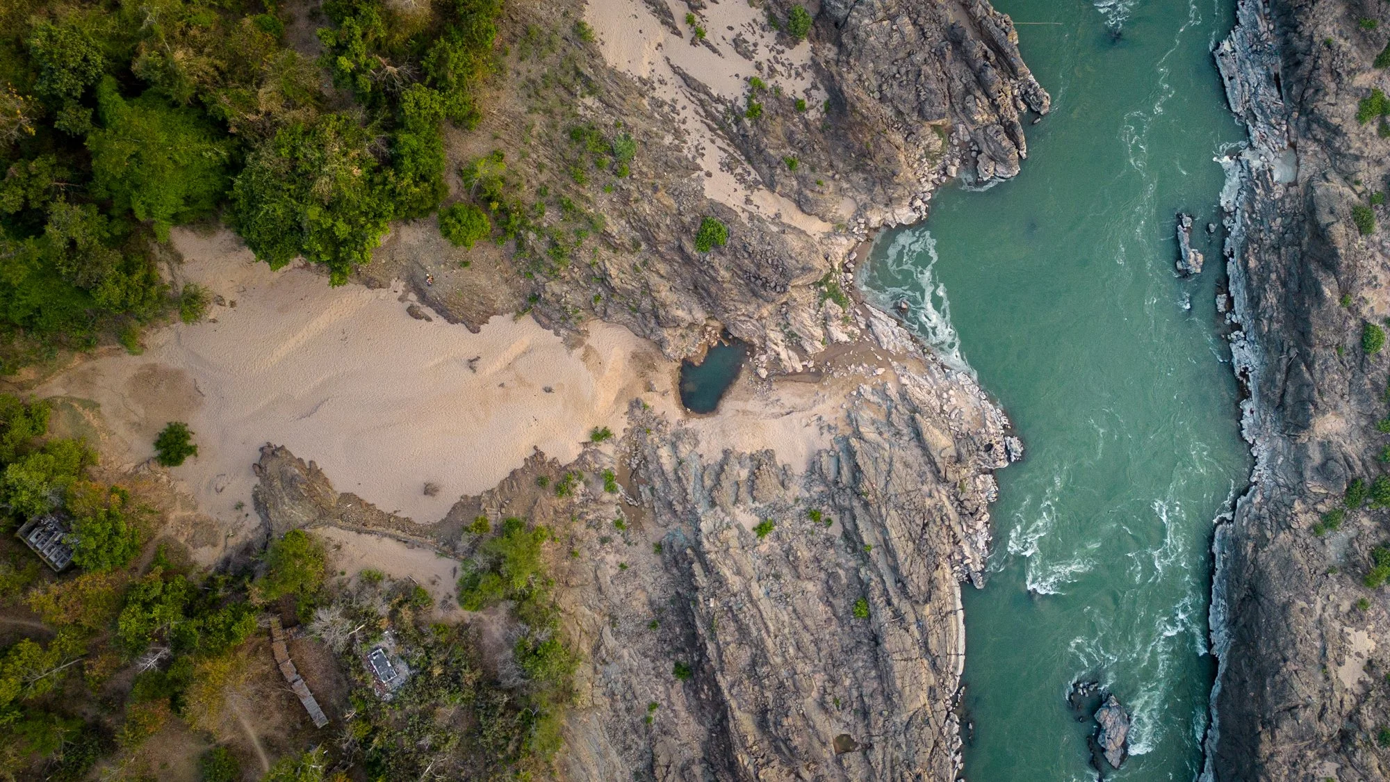 Aerial view of at the Mekong river flowing through a rocky canyon with a small sandy beach and green trees on one side.