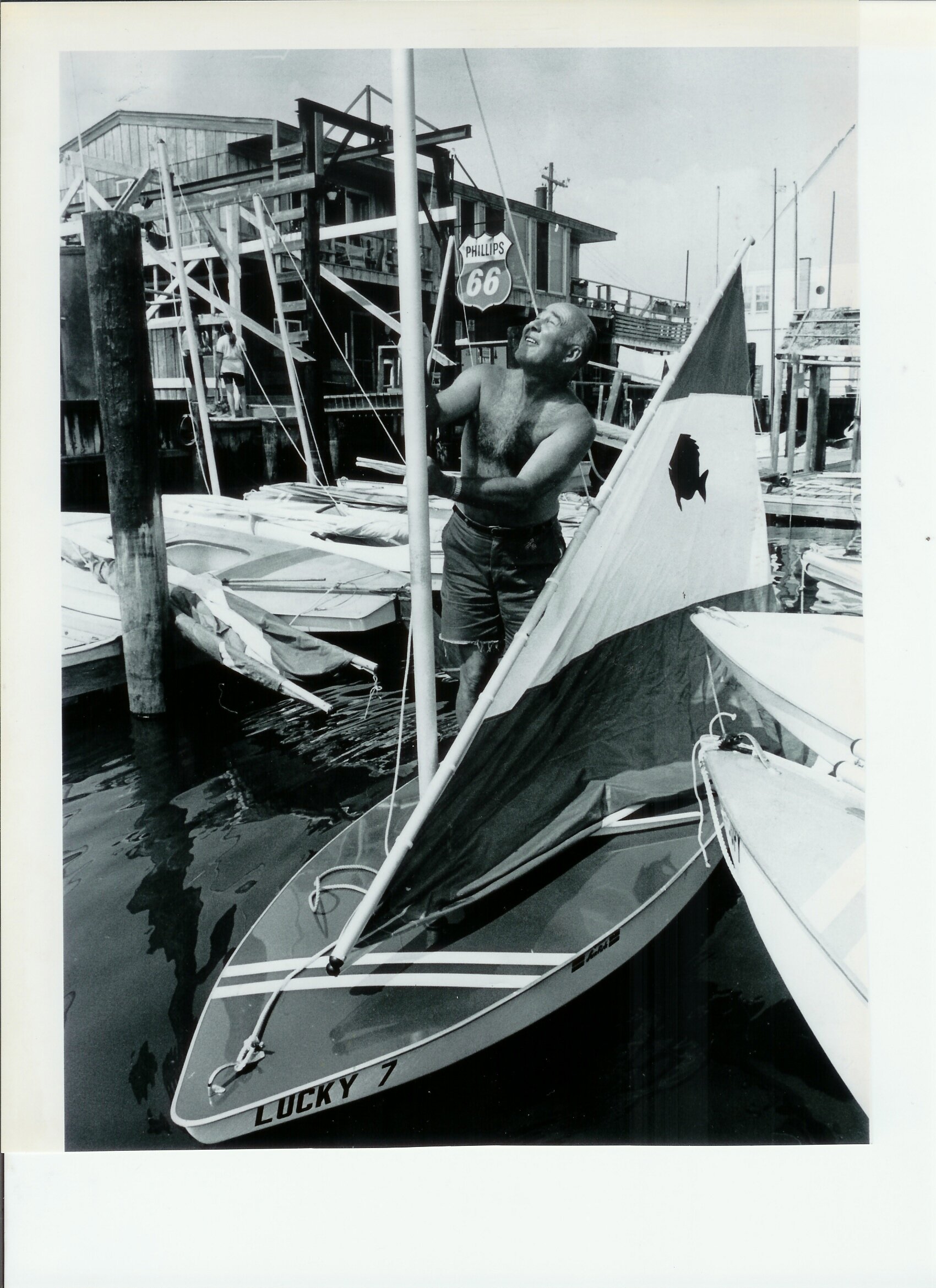 Dick Morgan makes a sail adjustment on a Sunfish in 1973. The Wharf and boat hoist are in the background.