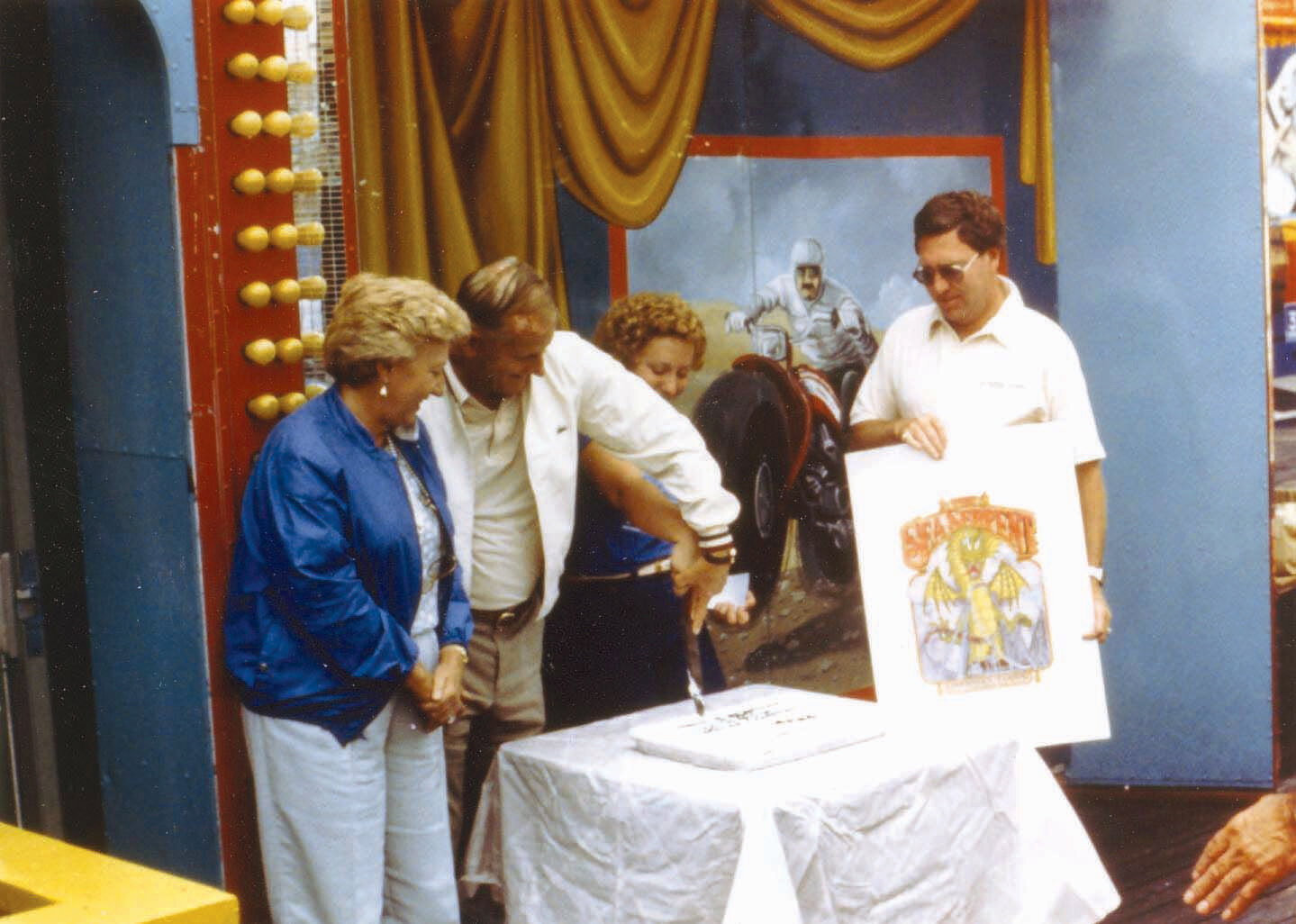 Will and Jackye Morey watch Barry Gehring cut the cake to celebrate the opening of the Sea Serpent roller coaster.