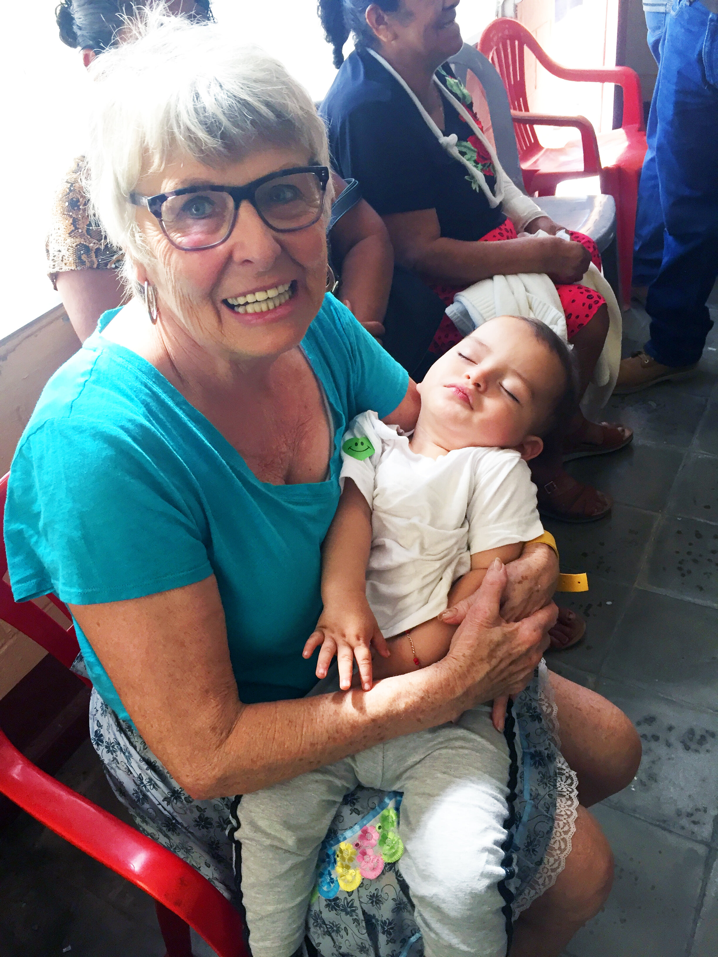 Eileen Buchanan holding a little boy while his mother is picking out sunglasses.