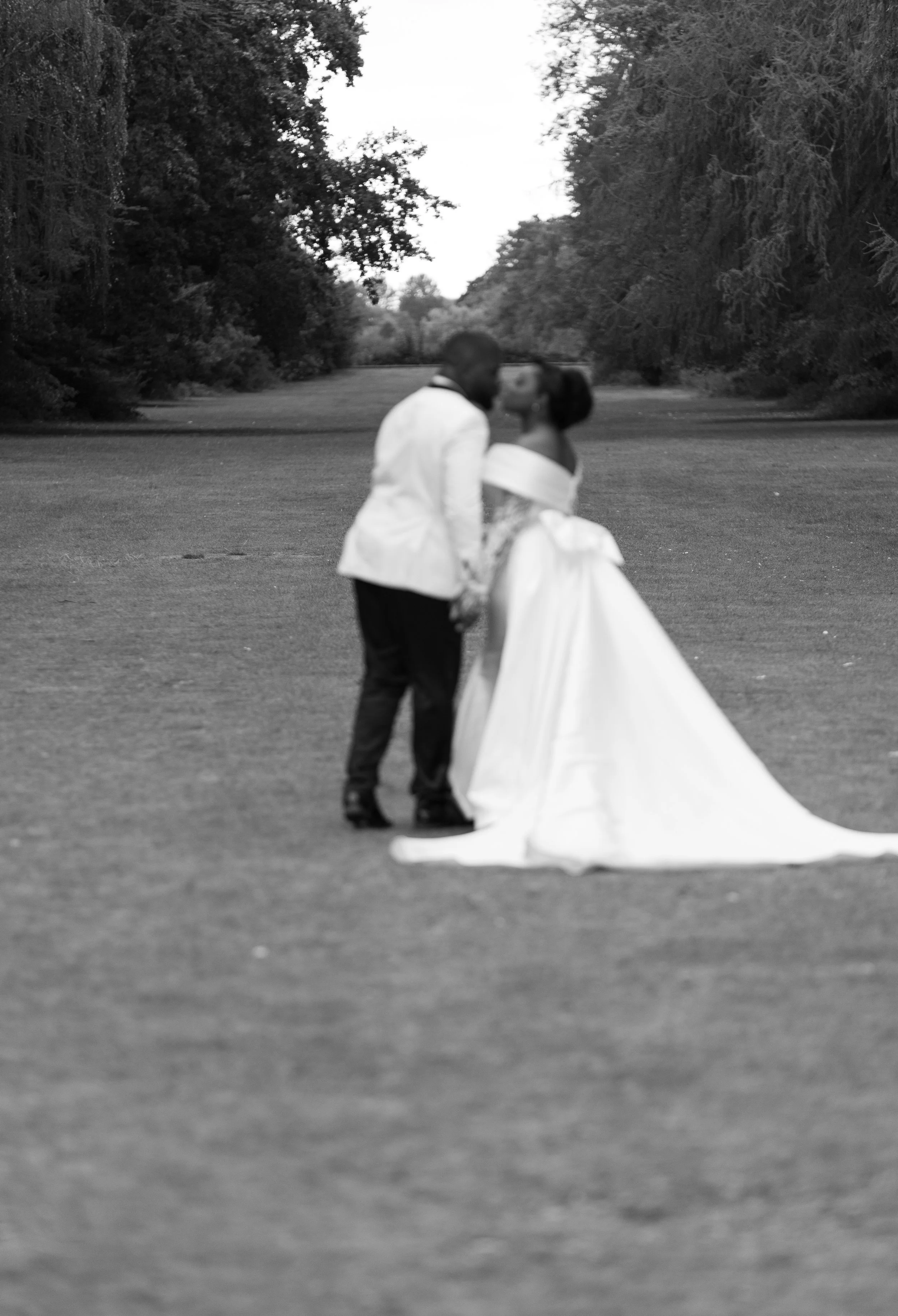 A couple dressed in wedding attire holding hands and looking at each other in a park with trees in the background.