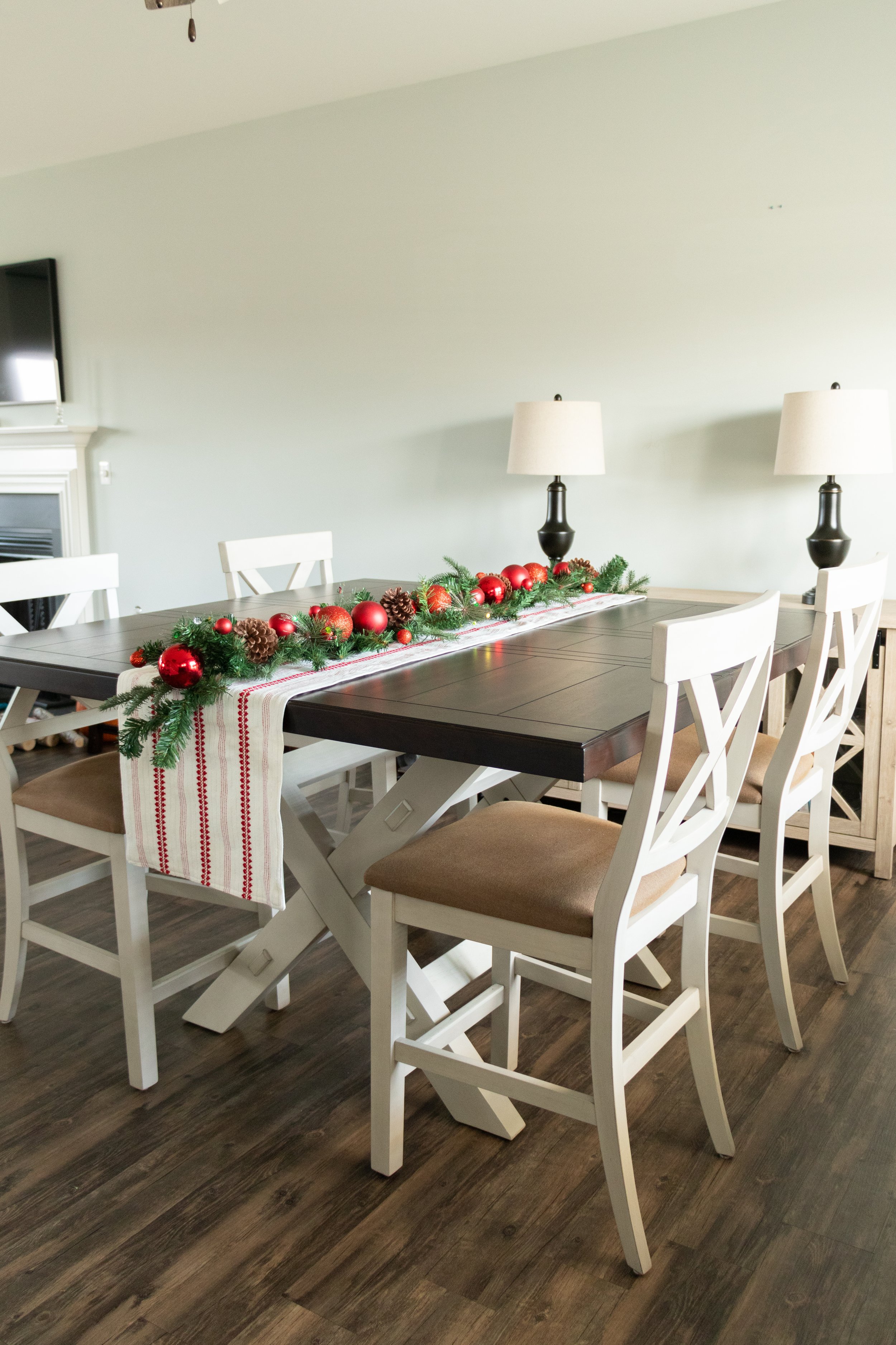 Large espresso farmhouse wooden dining room table with a simple red white table runner and a Christmas garland from Hobby Lobby 