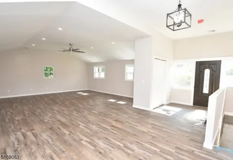 Empty living room with hardwood floors, white walls, ceiling fan, ceiling light, and front door with windows.