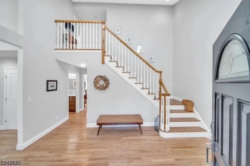 Living room with wooden staircase leading to an upper floor, a wooden bench against the wall, framed pictures on the wall, and hardwood floors.