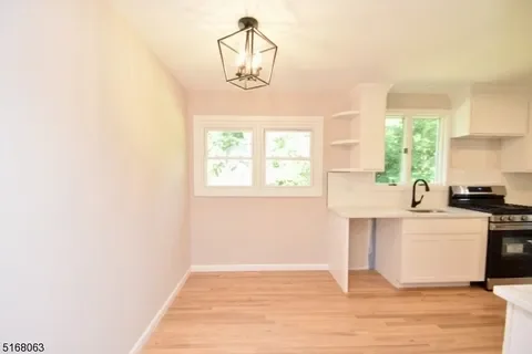 Empty dining area with a modern chandelier and kitchen in the background.