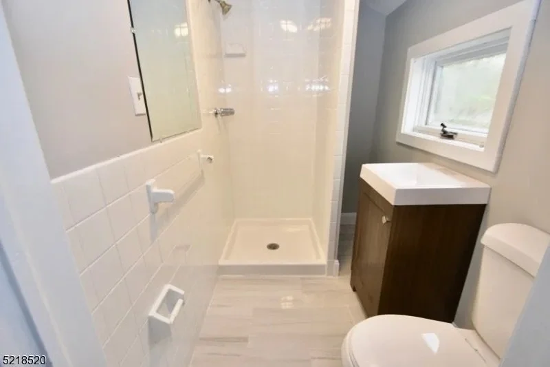 Small bathroom with a glass shower stall, a window, a dark wood vanity with a white sink, and a toilet.