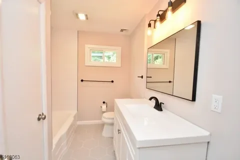 Bathroom with a white vanity, black fixtures, large mirror, toilet, and natural light from a window.