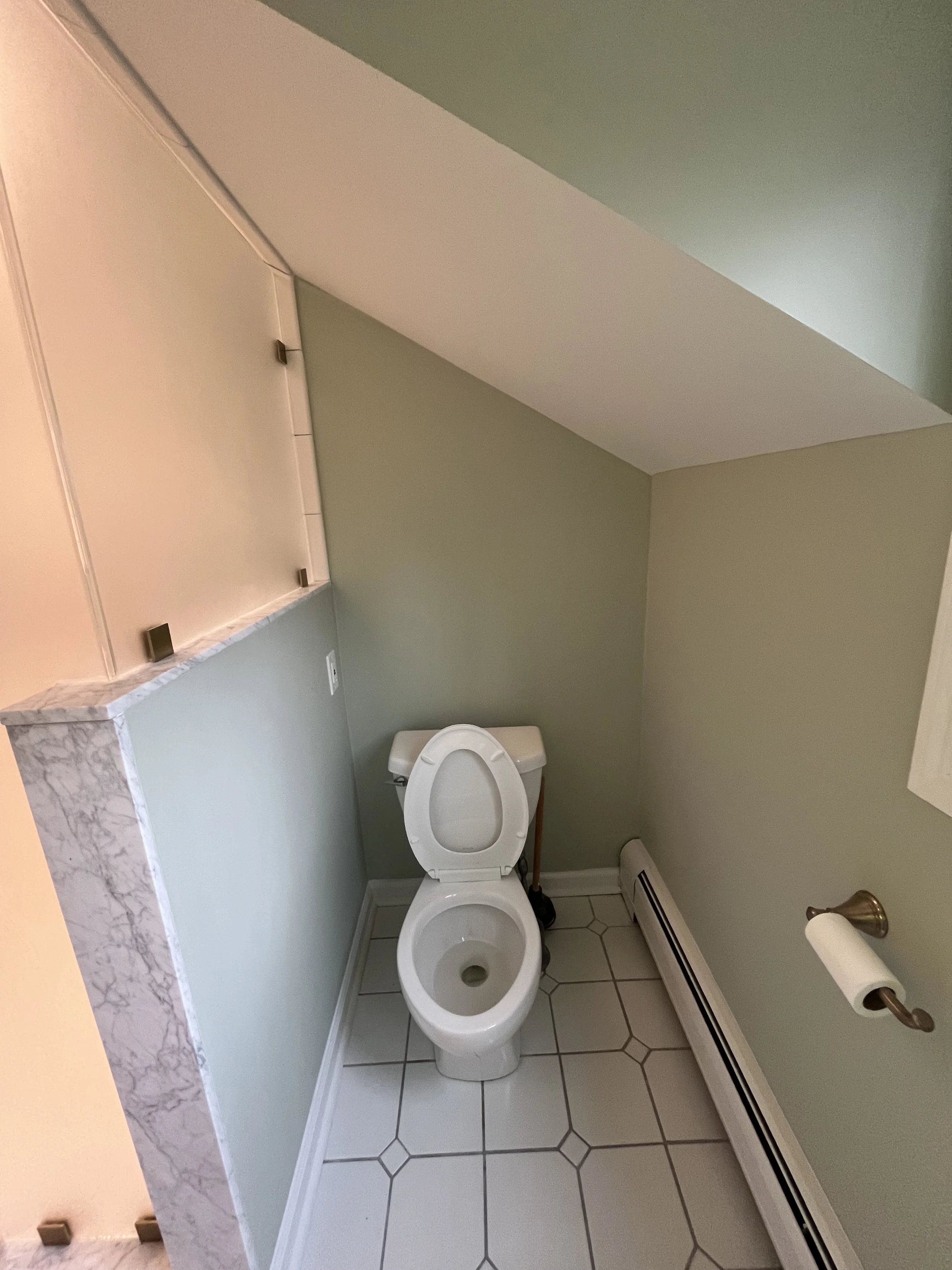 Small bathroom with a toilet, green walls, white tiled floor, and a toilet paper holder on the wall.