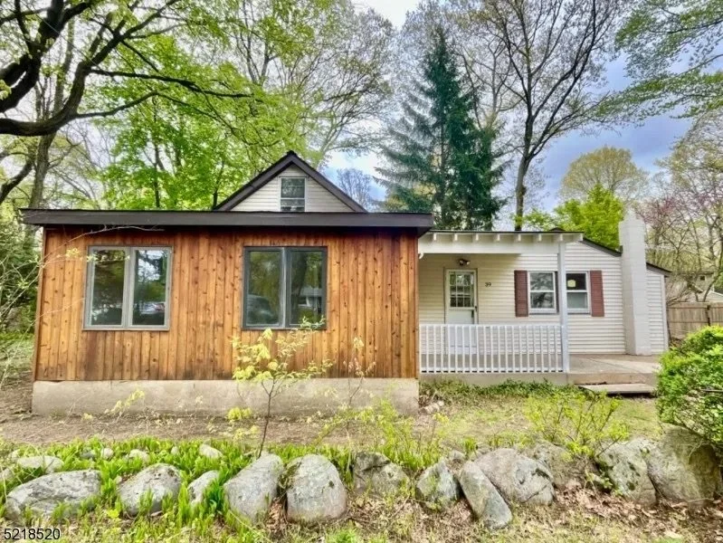 A split house with a wooden and white exterior, a porch, and surrounded by trees and rocks.